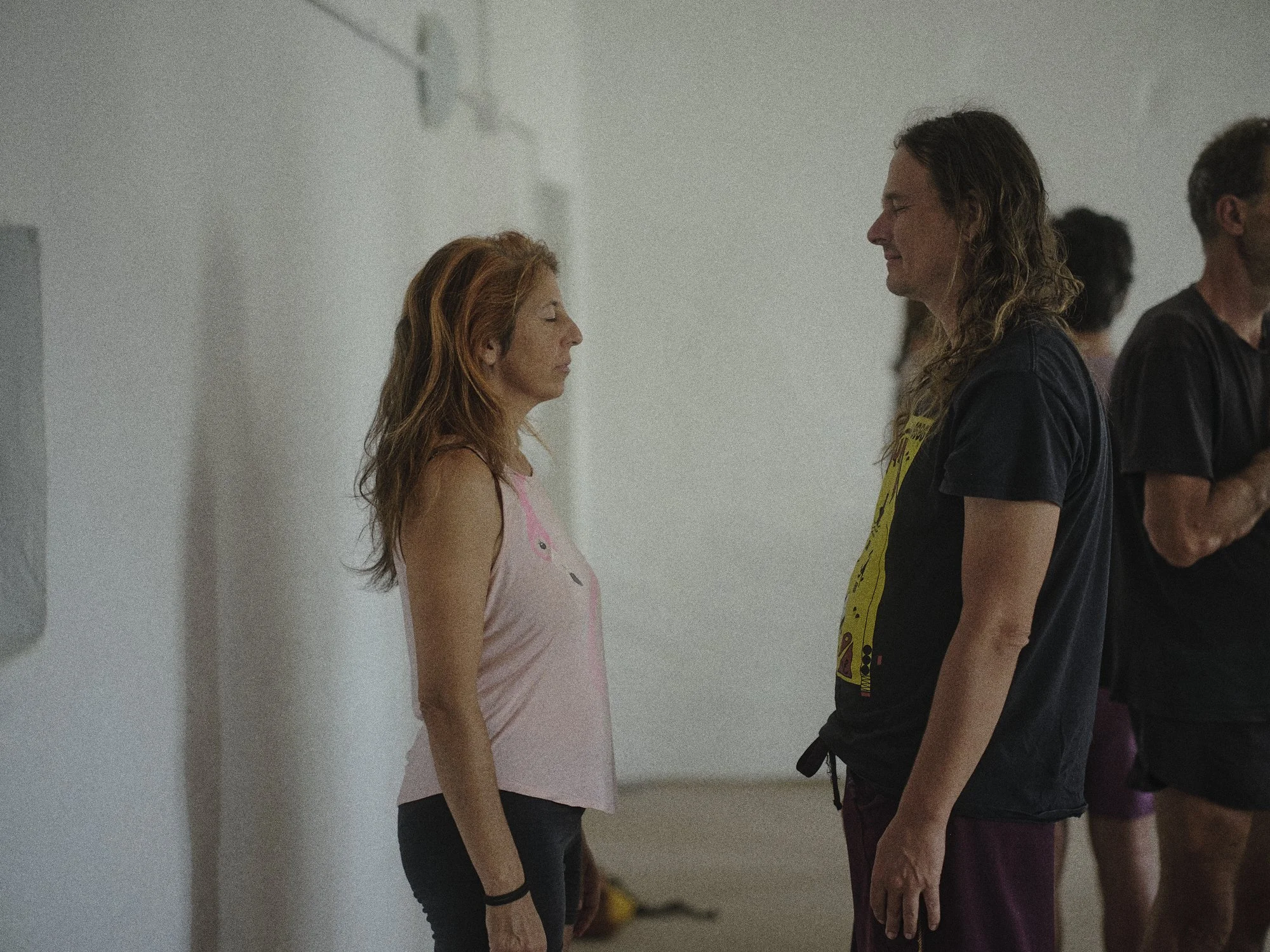 Dos personas, una mujer y un hombre, en una posición de meditación o introspección, se enfrentan con los ojos cerrados en un ambiente interior minimalista.