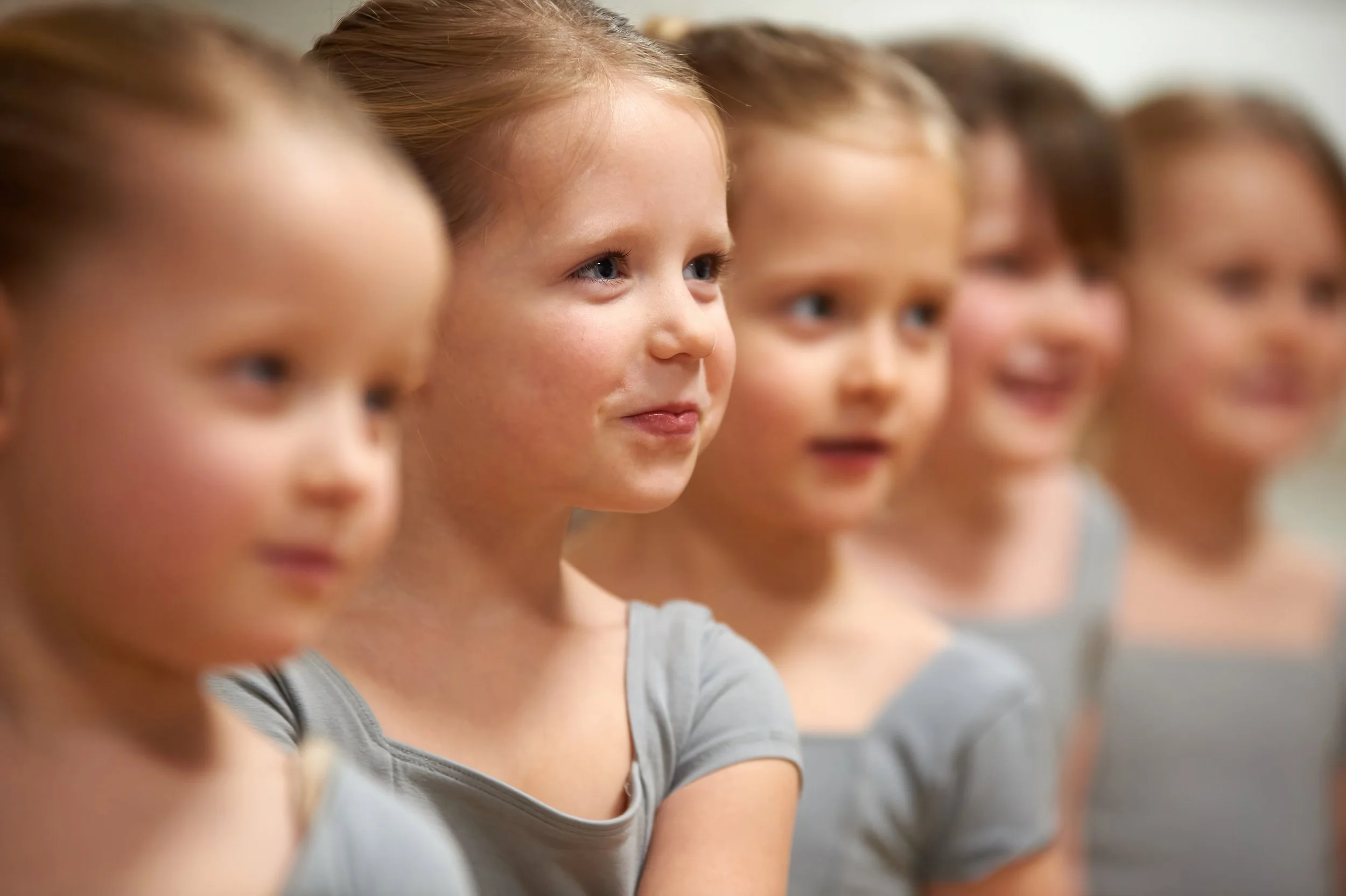 A group of young girls sitting in a row, attentively listening in a classroom or similar setting.