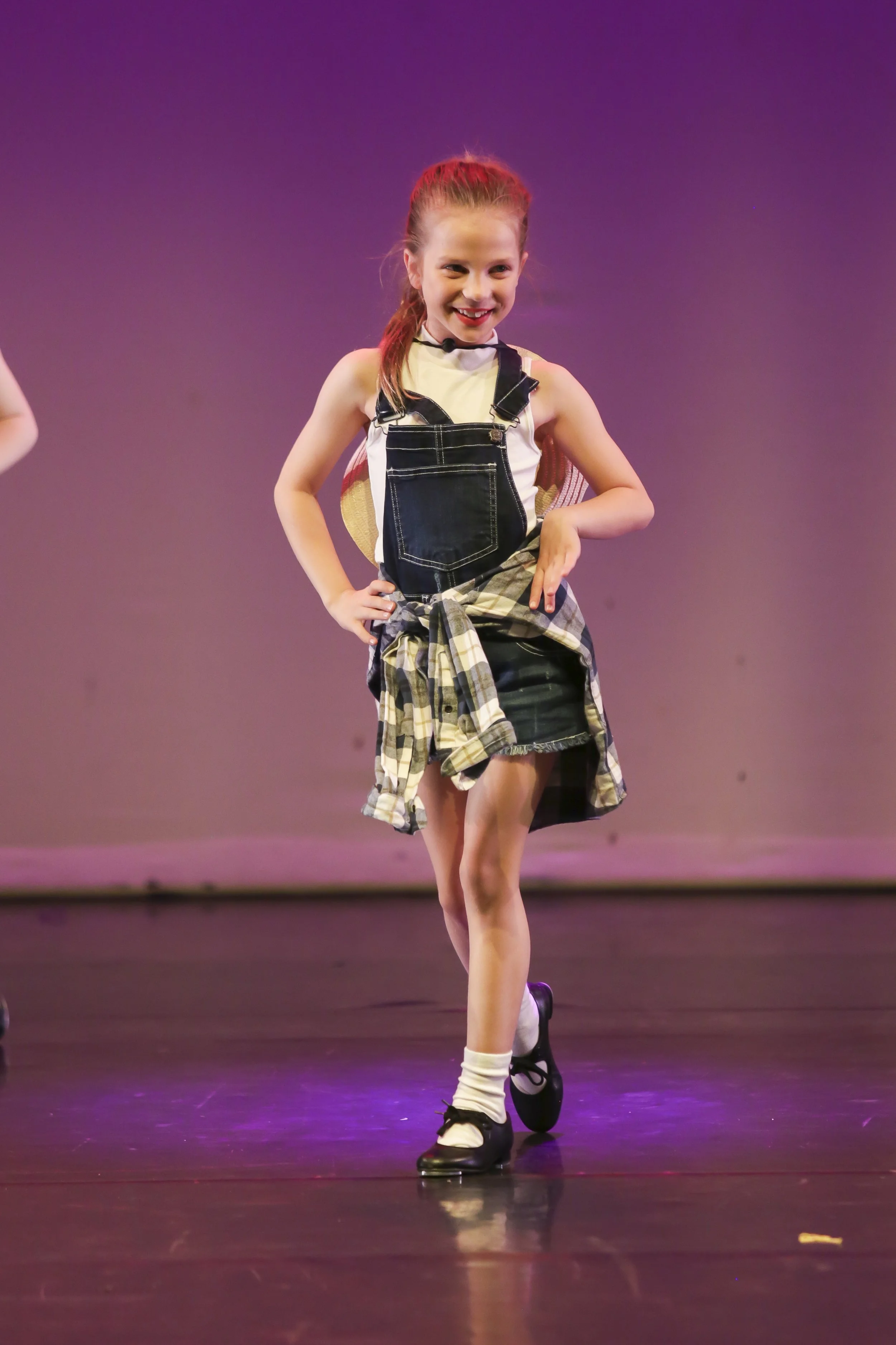 Young girl in a black and white dance costume performing on stage, smiling confidently with hands on her hips.