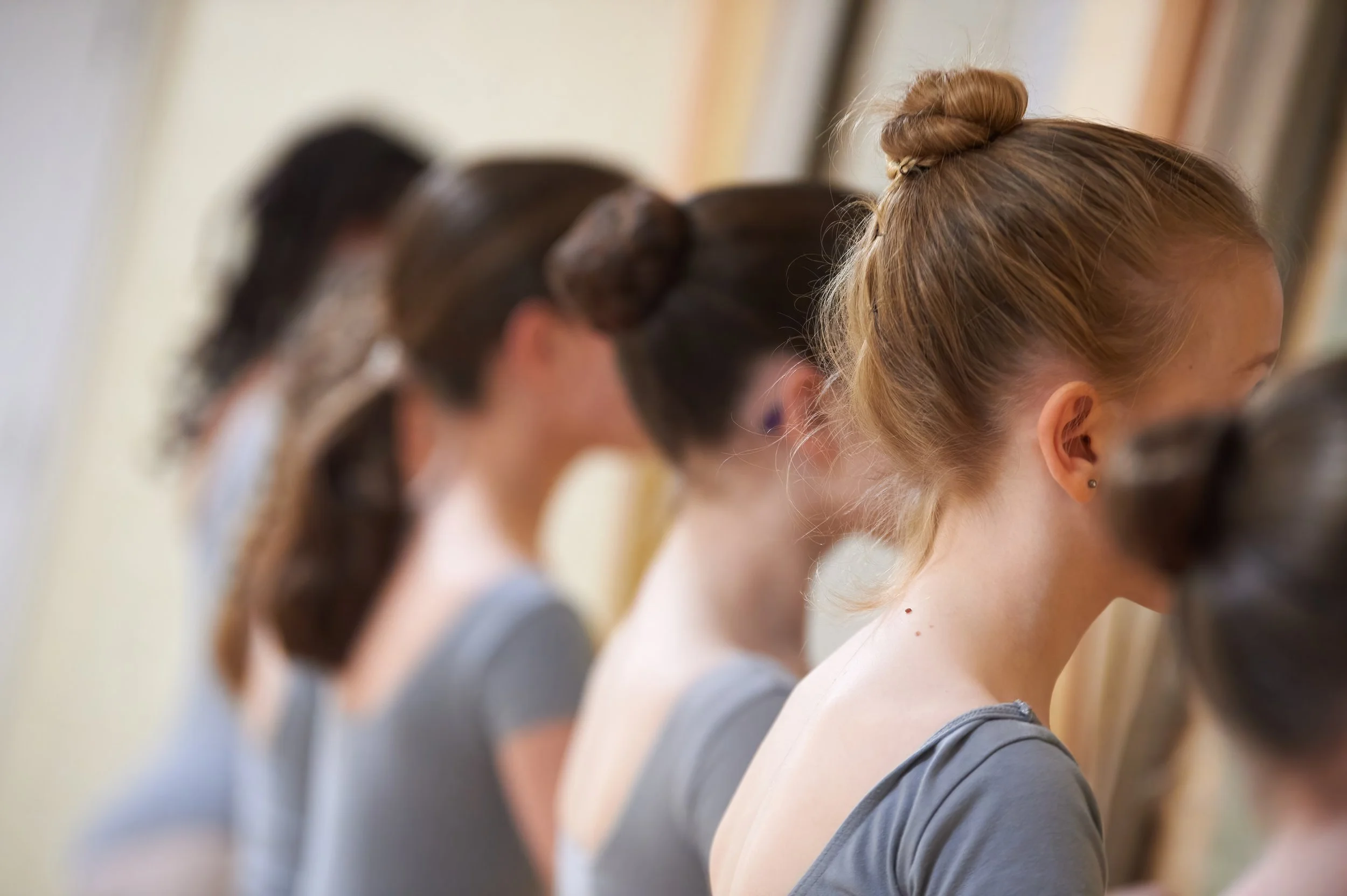 A row of young women with their heads bowed, focusing on their activities, tied or styled hair, and casual clothing.