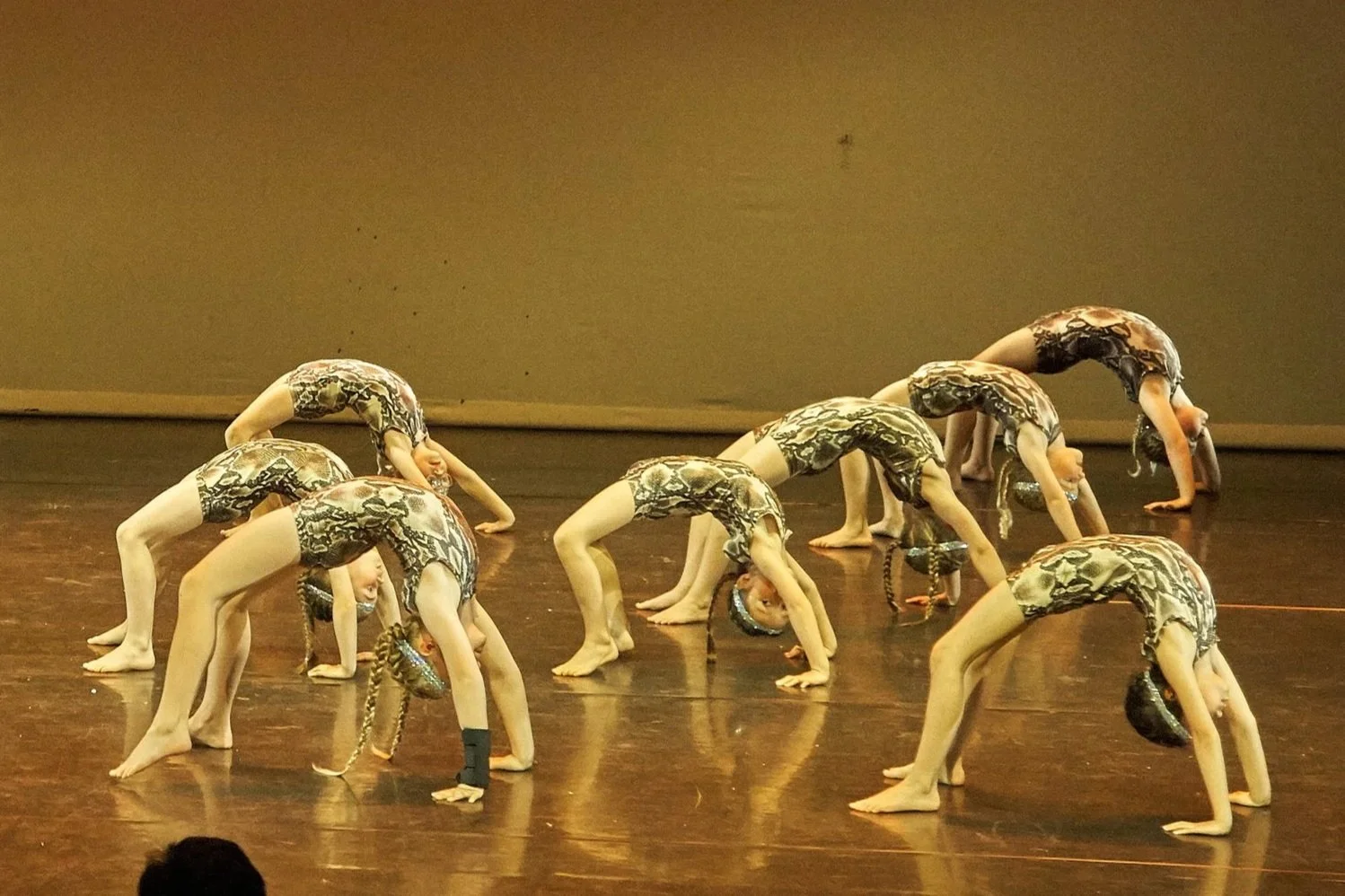 Group of young girls in matching costumes performing a backbend dance pose on stage.