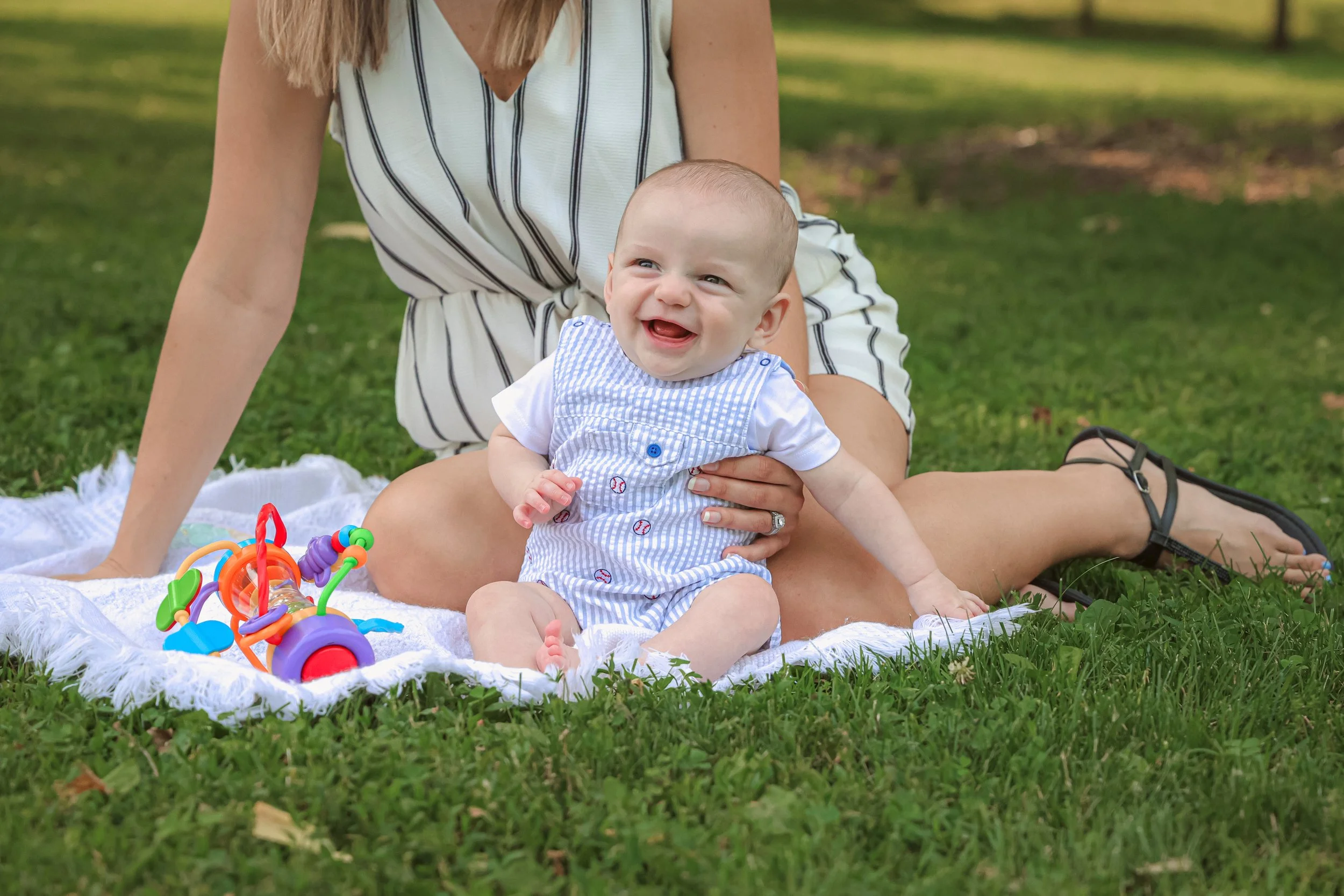 A mom holding her giggling baby during family photo session in the summer at a park captured by Indianapolis family photographer