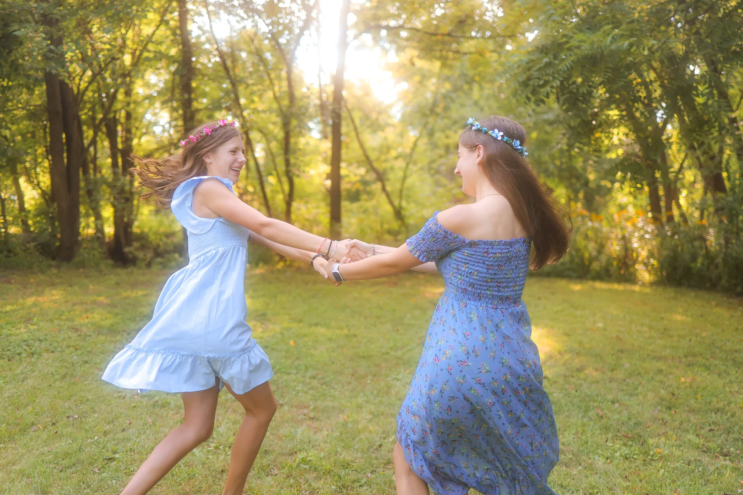 Two young women in blue dresses holding hands and spinning in a park during portrait session