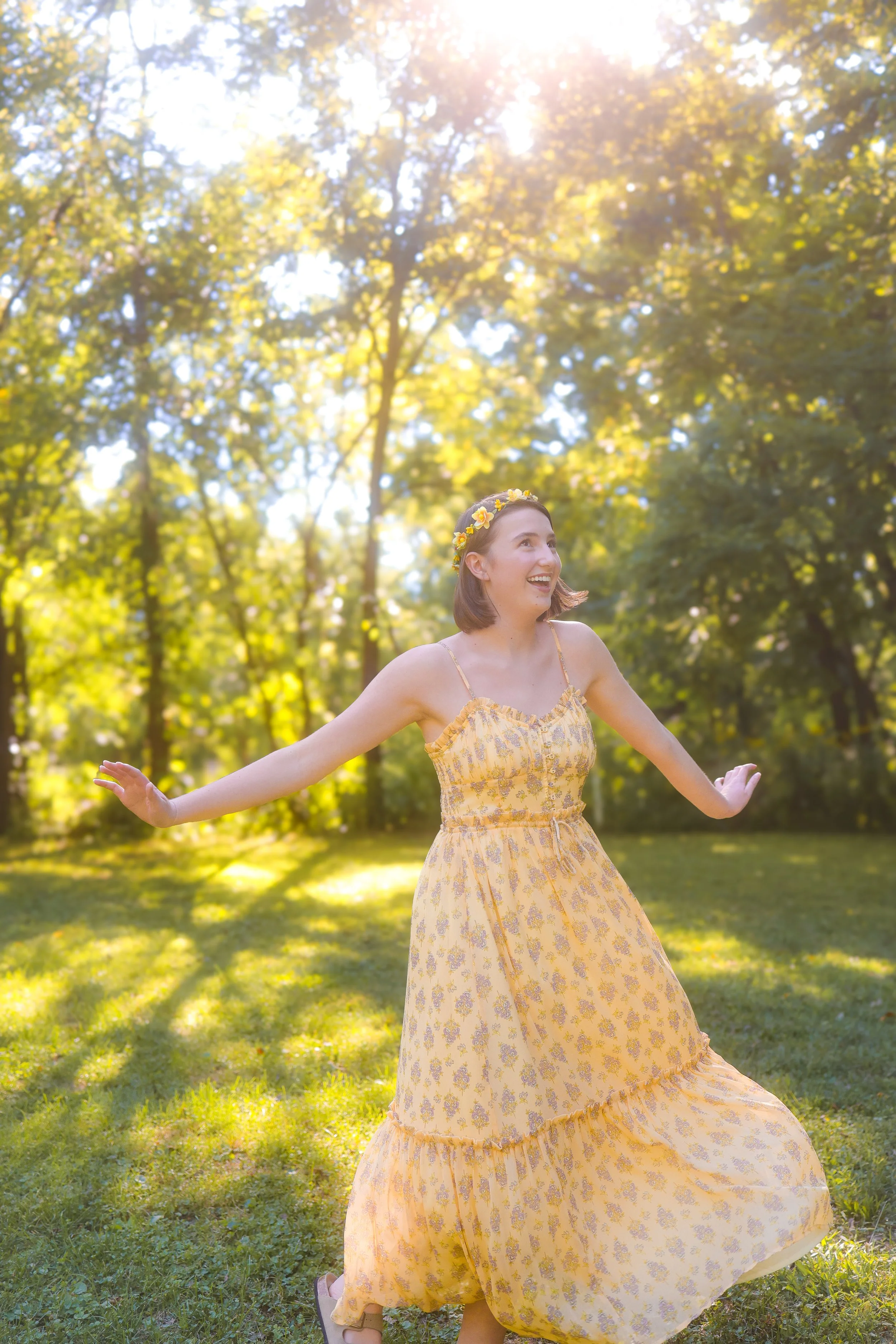 A young woman twirling and smiling and dancing outdoors in a sunny park during portrait photography session
