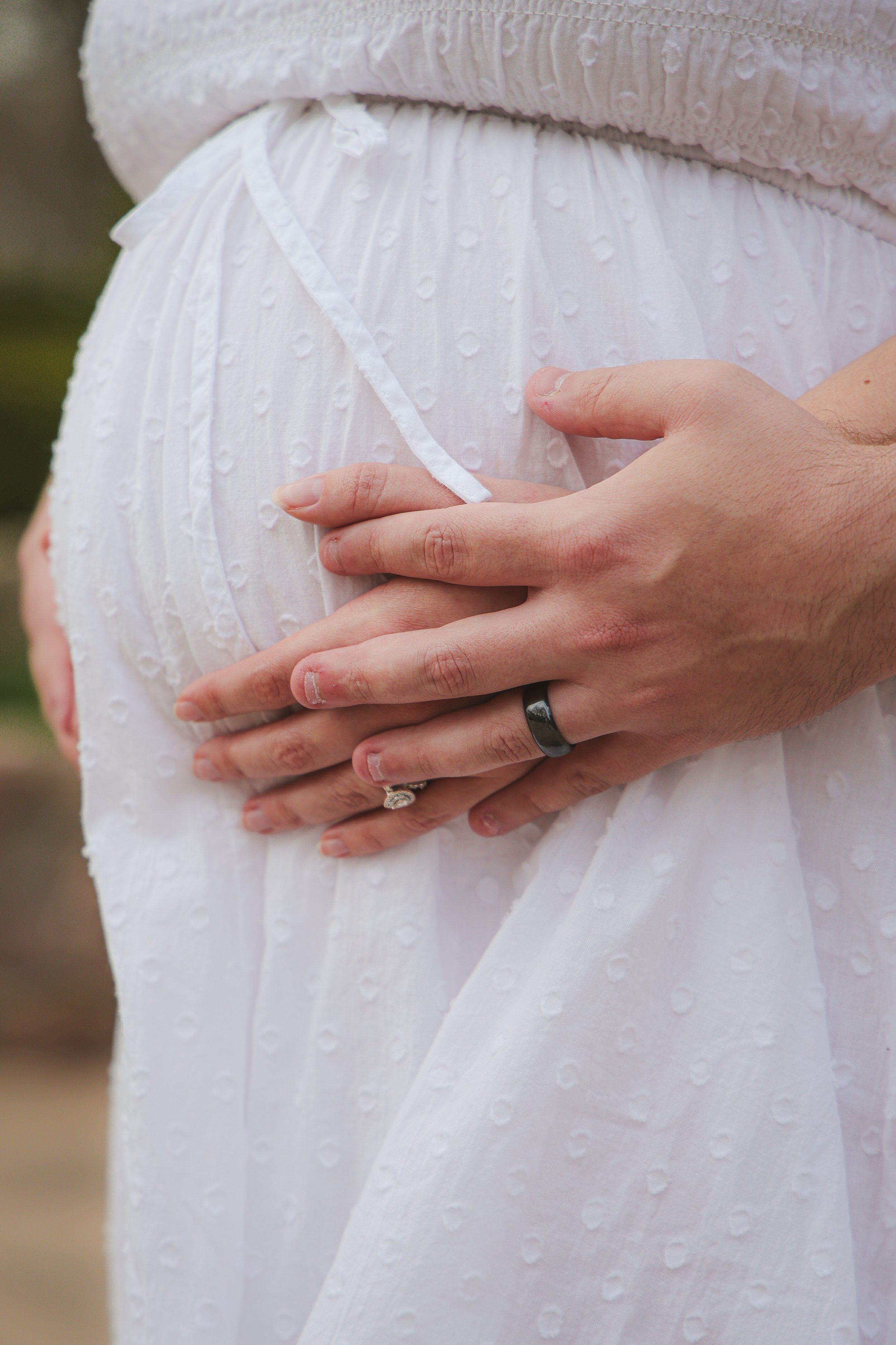 A pregnant woman with husband holding her belly during maternity photo session in the summer time for Indianapolis family photographer at an outdoor park in Carmel, Indiana