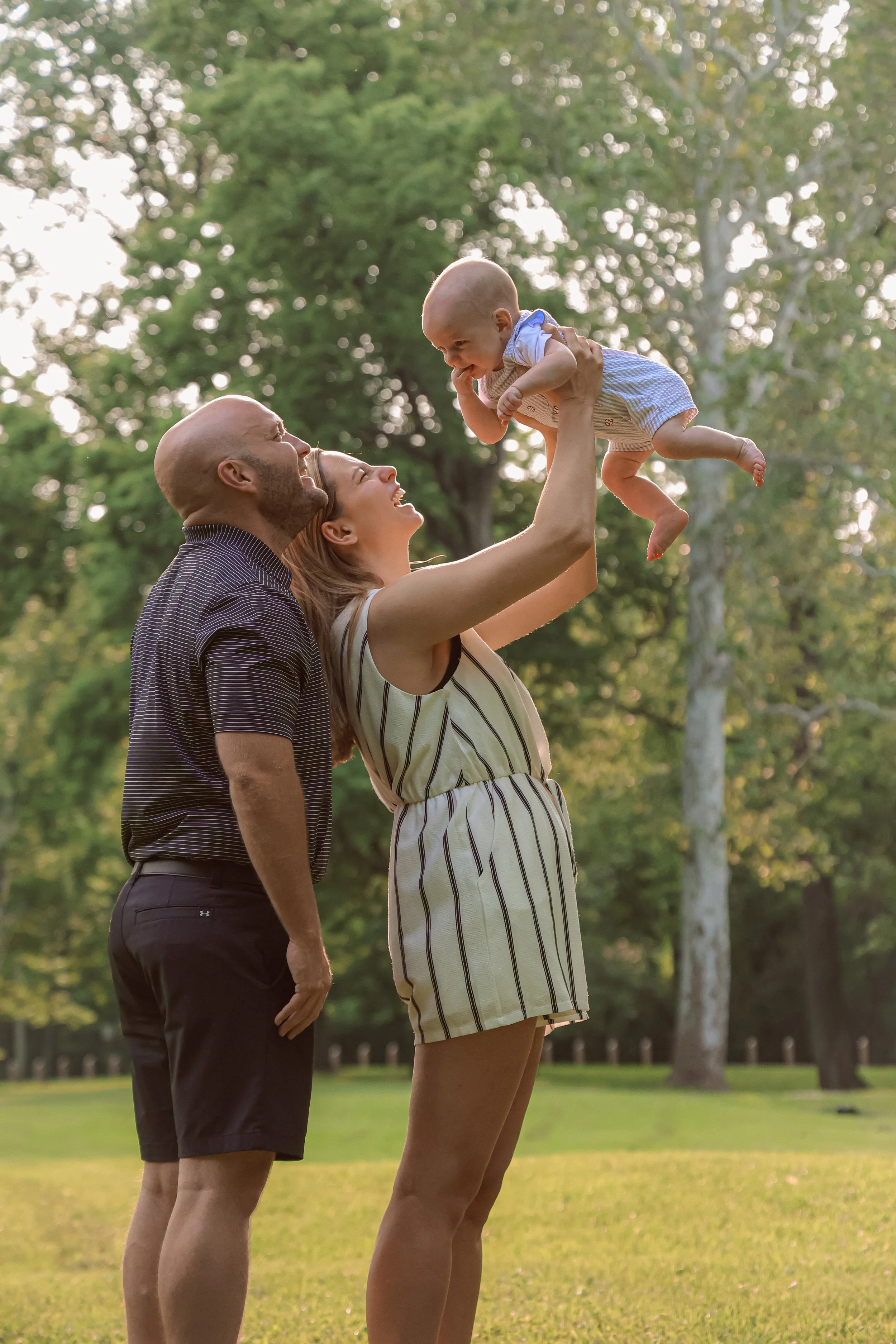 A mom and dad playing with their baby during family photo session in the summer at a park captured by Indianapolis family photographer