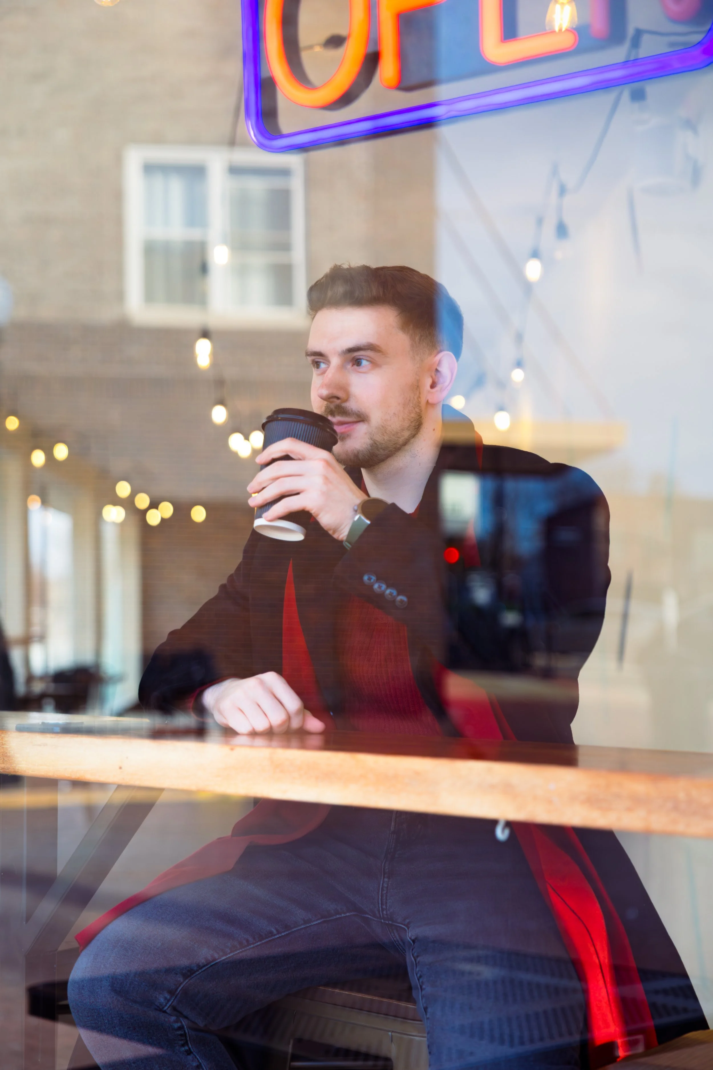 Indianapolis portrait session of a man drinking coffee through a window of a coffee shop. 