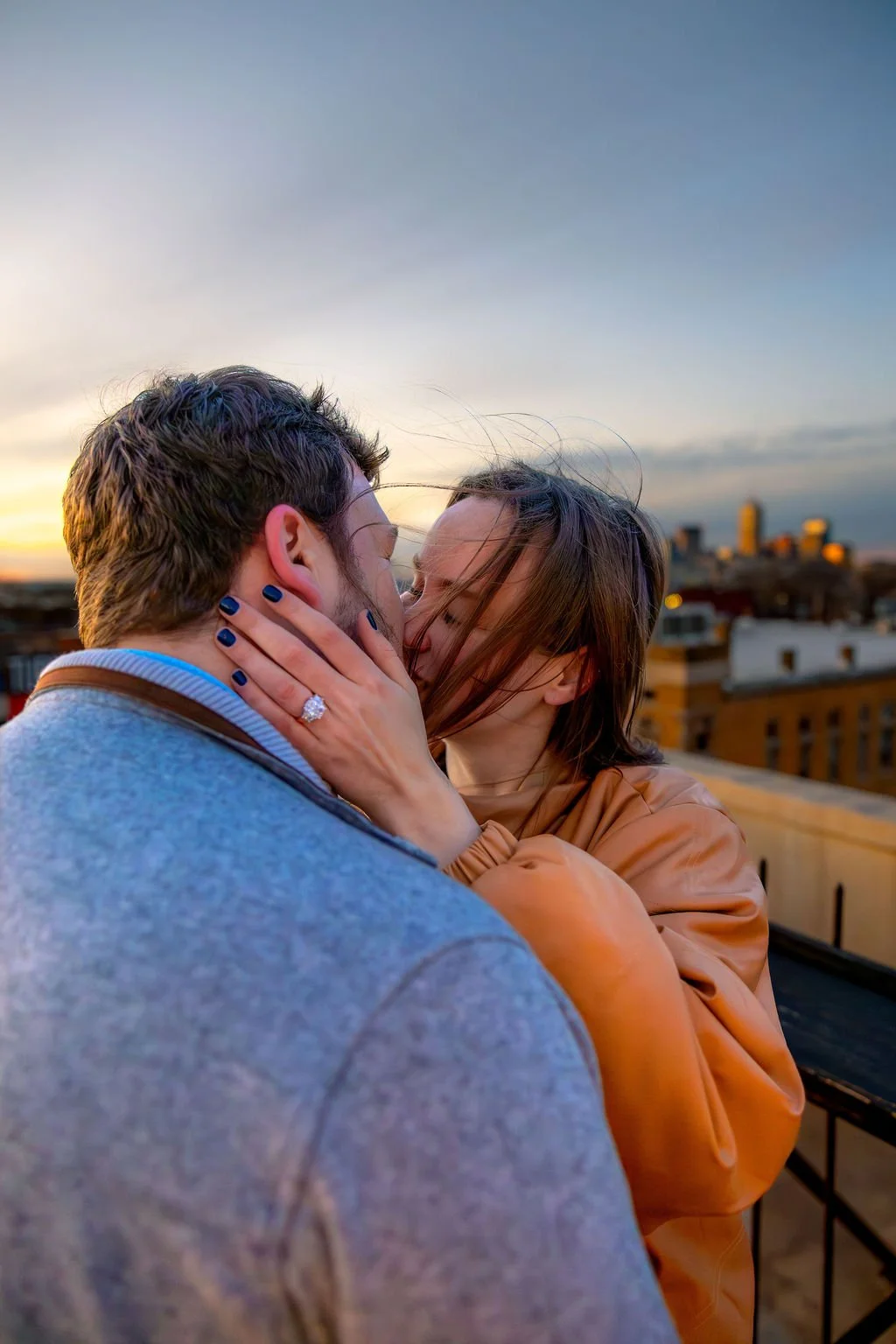 A couple sharing a kiss on a rooftop during sunset with Indianapolis buildings in the background after proposal.