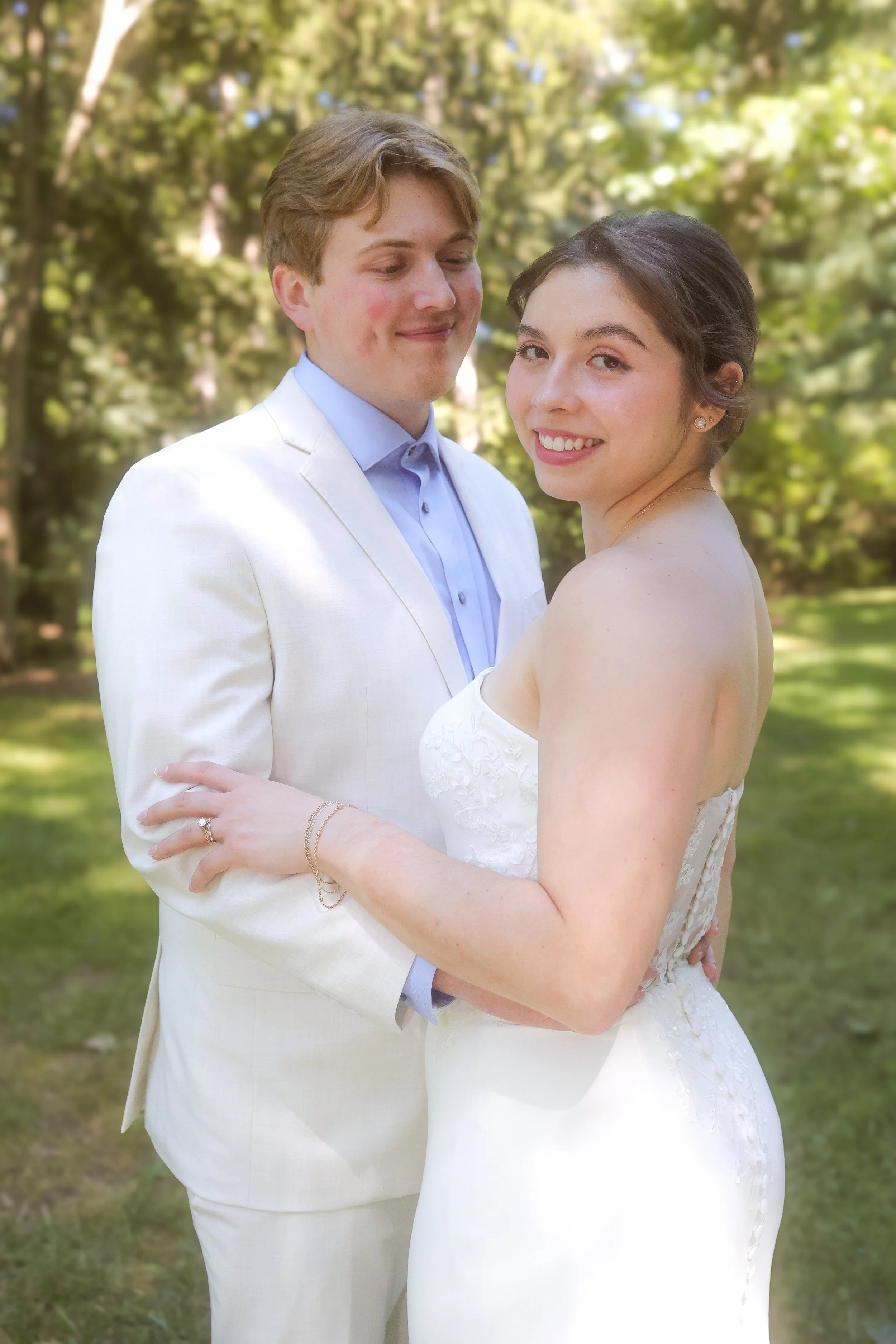 A groom holding his bride looking lovingly at her as she smiles at the camera in summer outdoor wedding ceremony captured by wedding photographer in Indianapolis