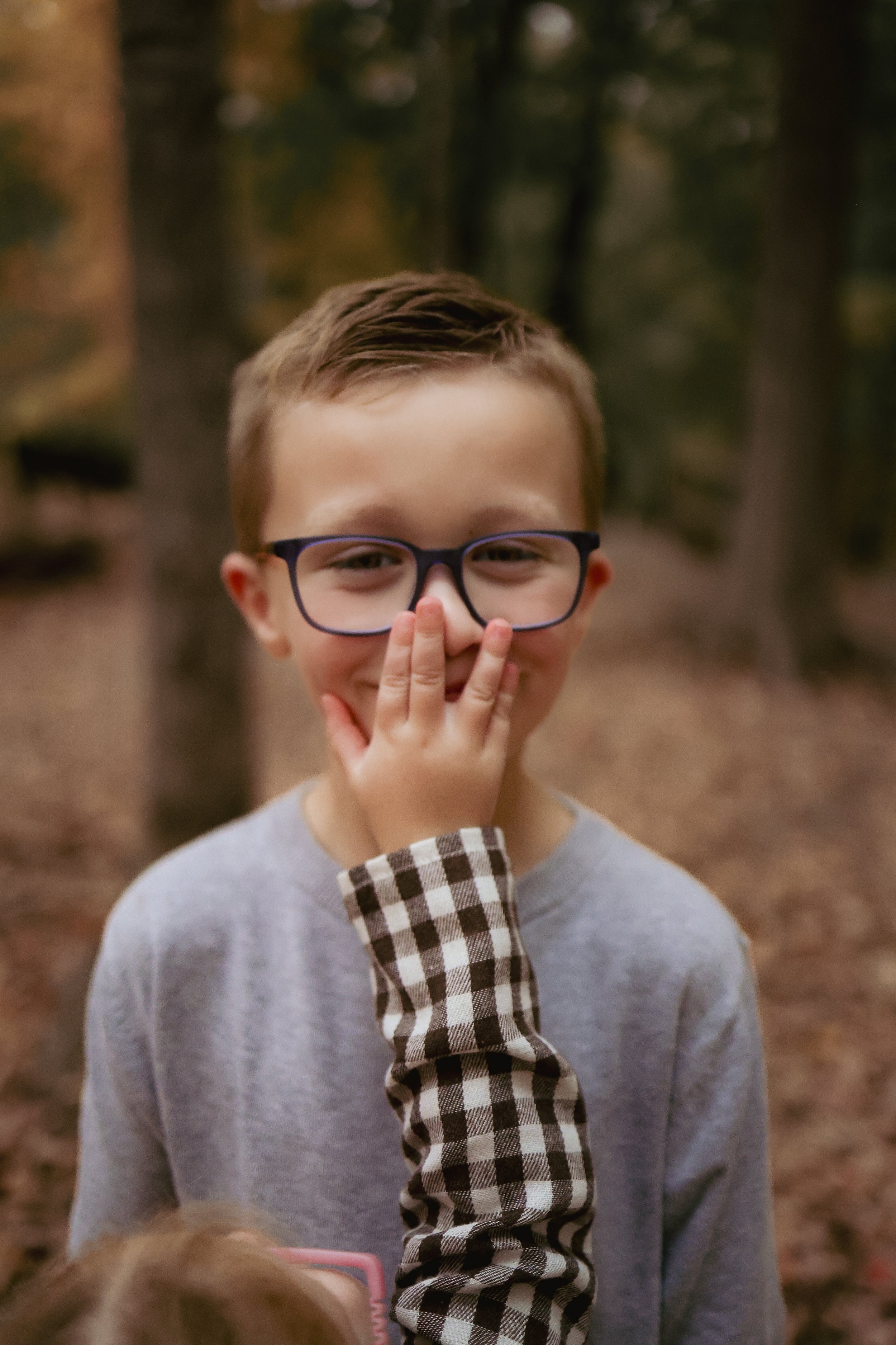 Funny photo of young boy smiling for Indianapolis family photographer during family photo session in the fall at a park in Indianapolis