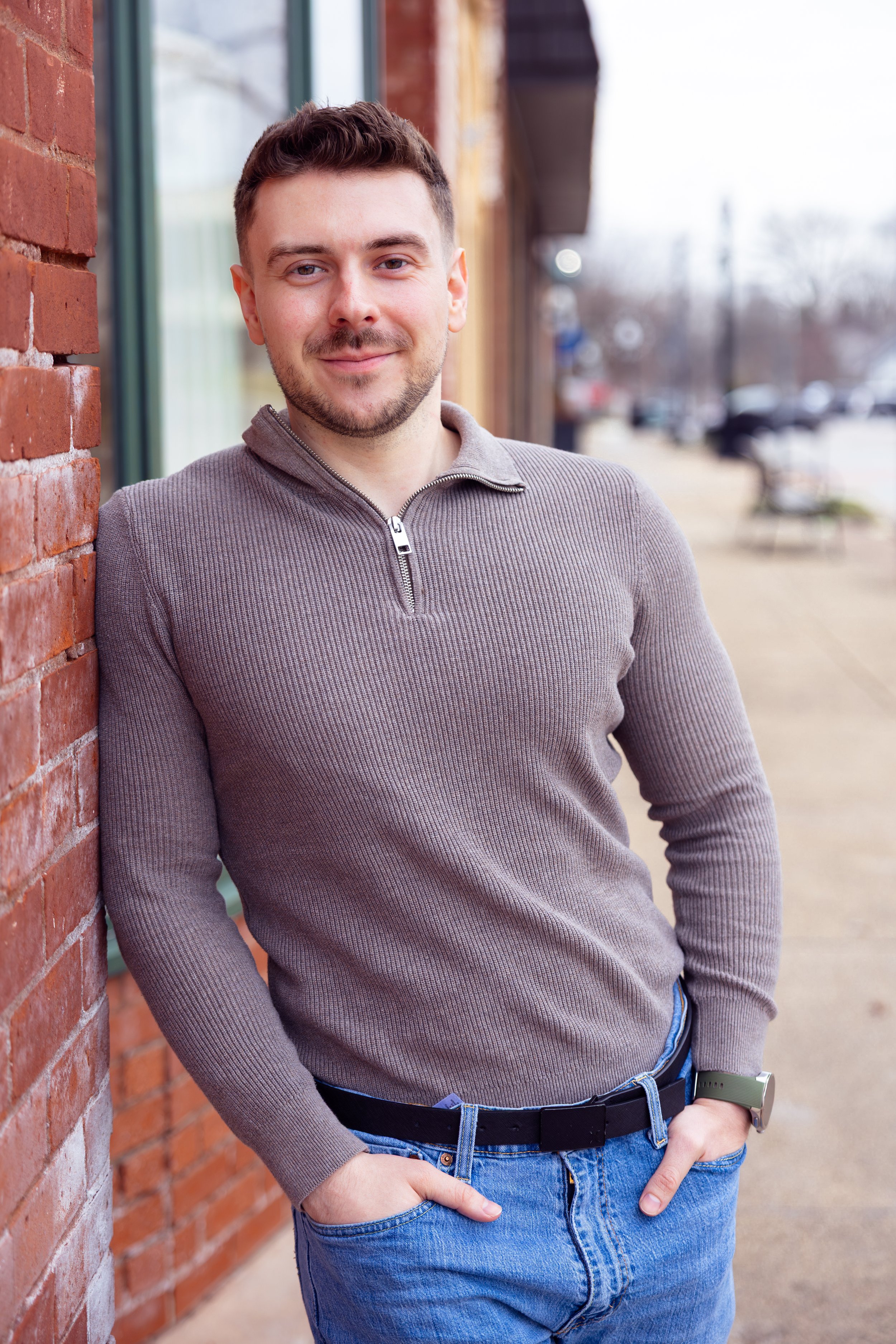 Indianapolis portrait session of a young man leaning against a brick wall with a gentle smile outdoors in winter