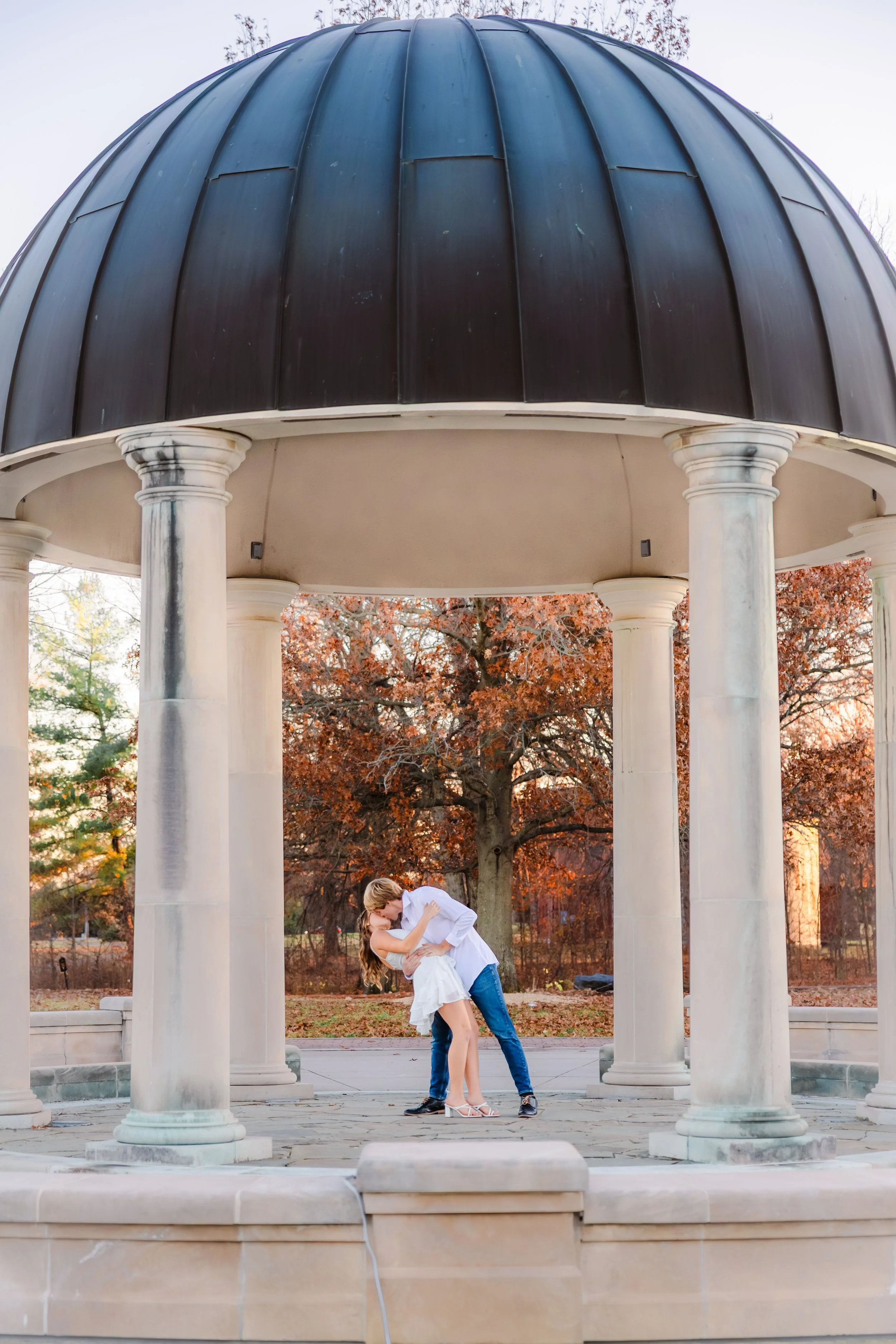 Engaged couple kiss under gazebo during engagement photography session with Indianapolis engagement photographer at a park in Carmel, Indiana in the fall season