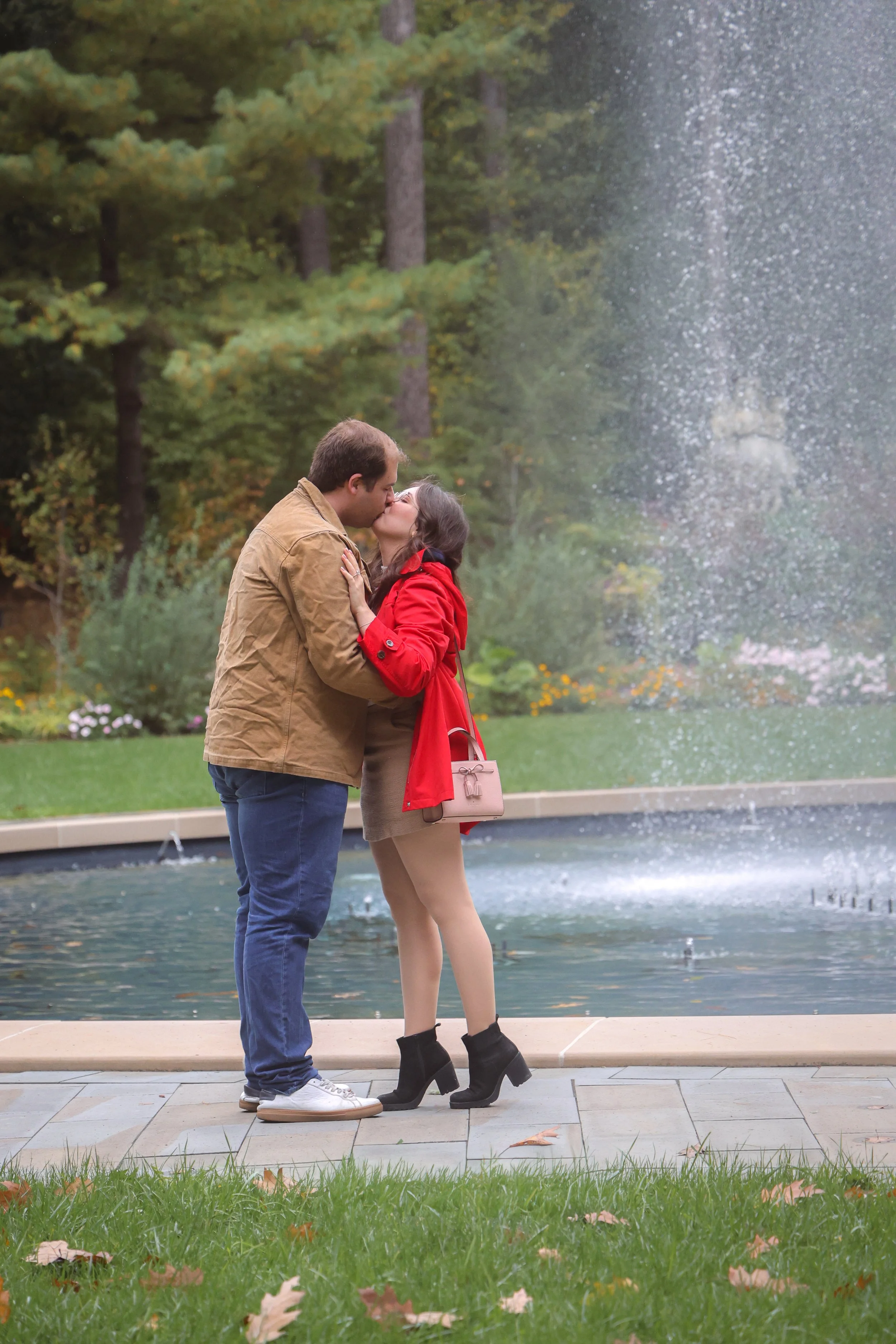 engaged couple kiss in front of a fountain in the rain in Indianapolis during proposal photo session, captured by Indianapolis proposal photographer