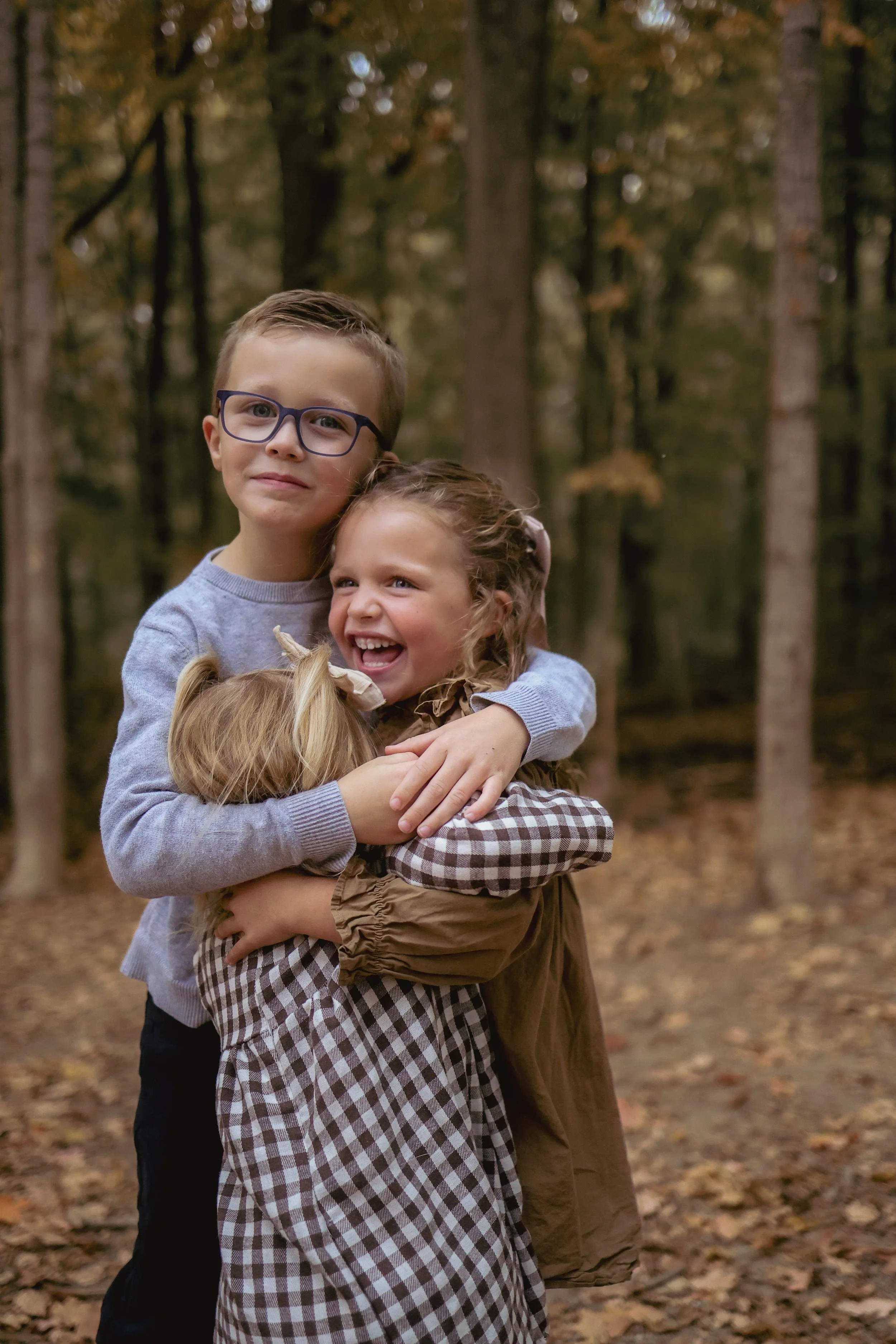 Young siblings smiling for Indianapolis family photographer during family photo session in the fall at a park in Indianapolis