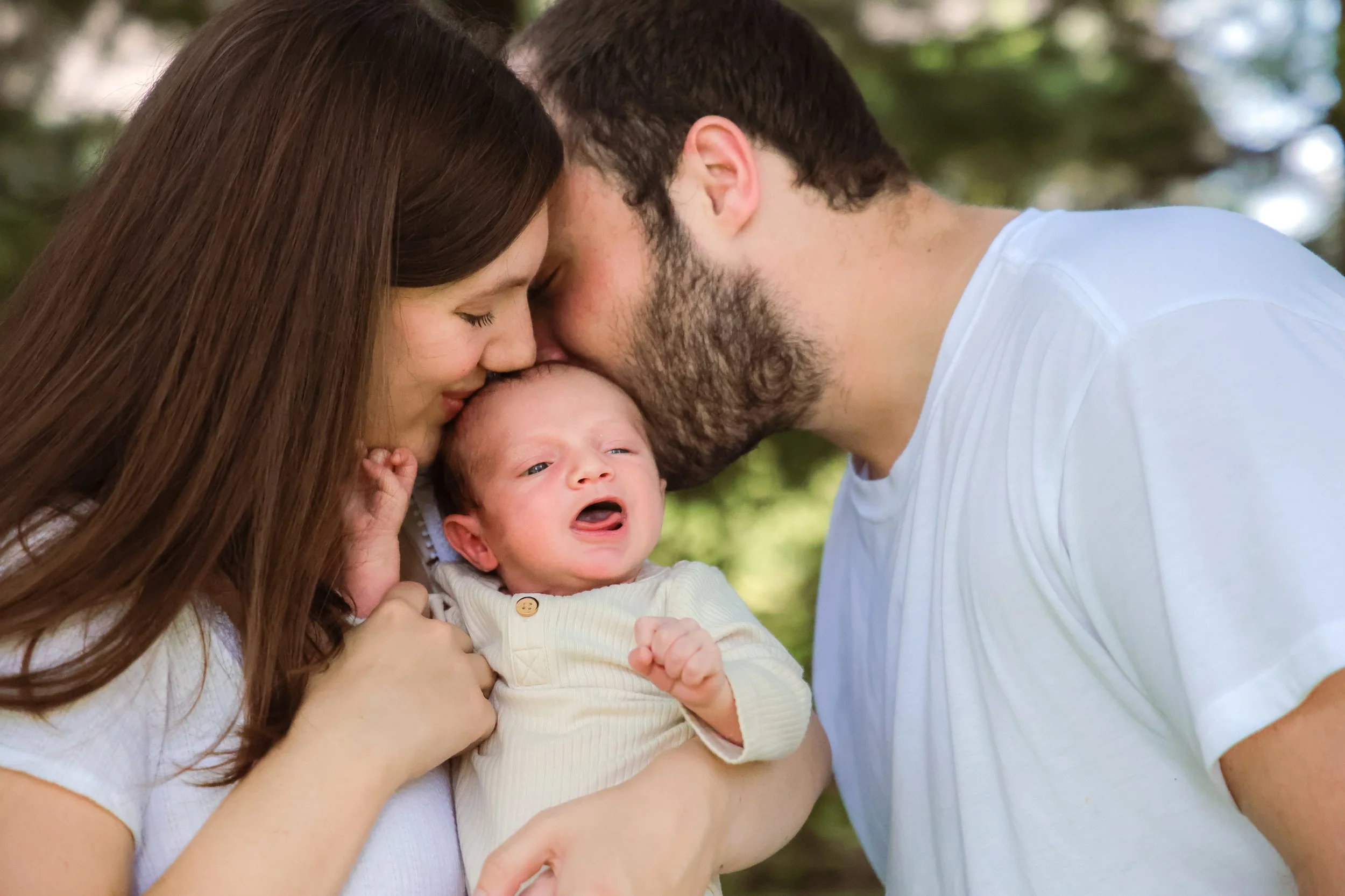 A man and wife kissing their newborn infant during family photo session in the summer time captured by Indianapolis family photographer in Westfield, Indiana