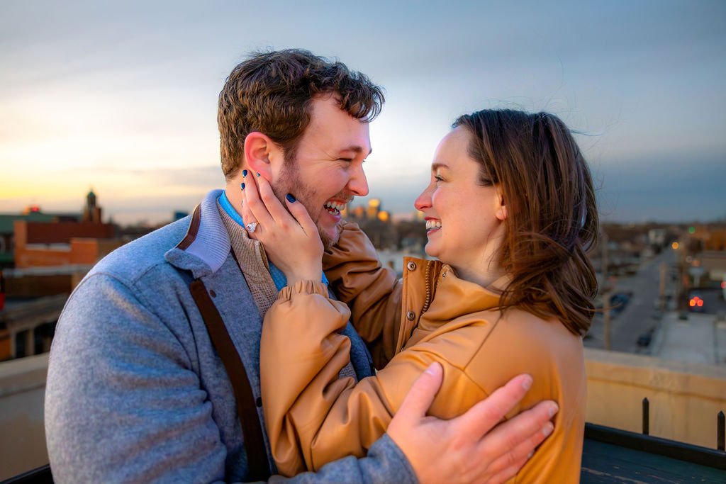 A couple smiling and holding each other on a rooftop during sunset.