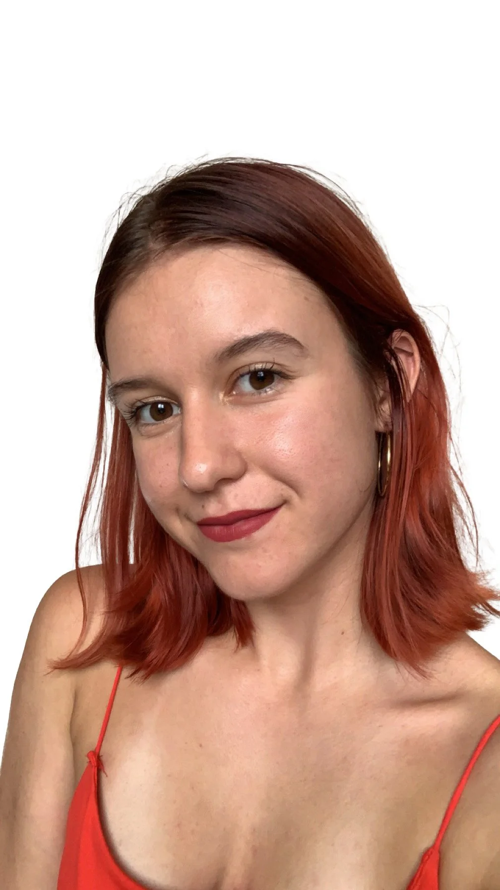 Une jeune femme avec des cheveux rouges, portant un haut rouge à fines bretelles, souriant devant un fond blanc.