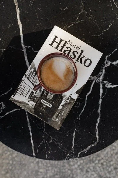 A book titled "Hasko" by Marek Hasko placed on a black marble table, with a cup of coffee on top of the book.