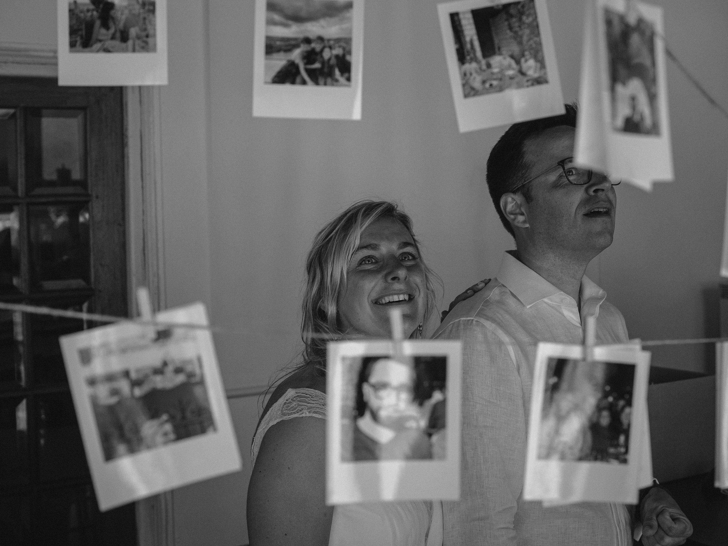 Une scène en noir et blanc avec deux personnes, une femme souriante et un homme portant des lunettes, qui regardent des photos suspendues avec des pinces.