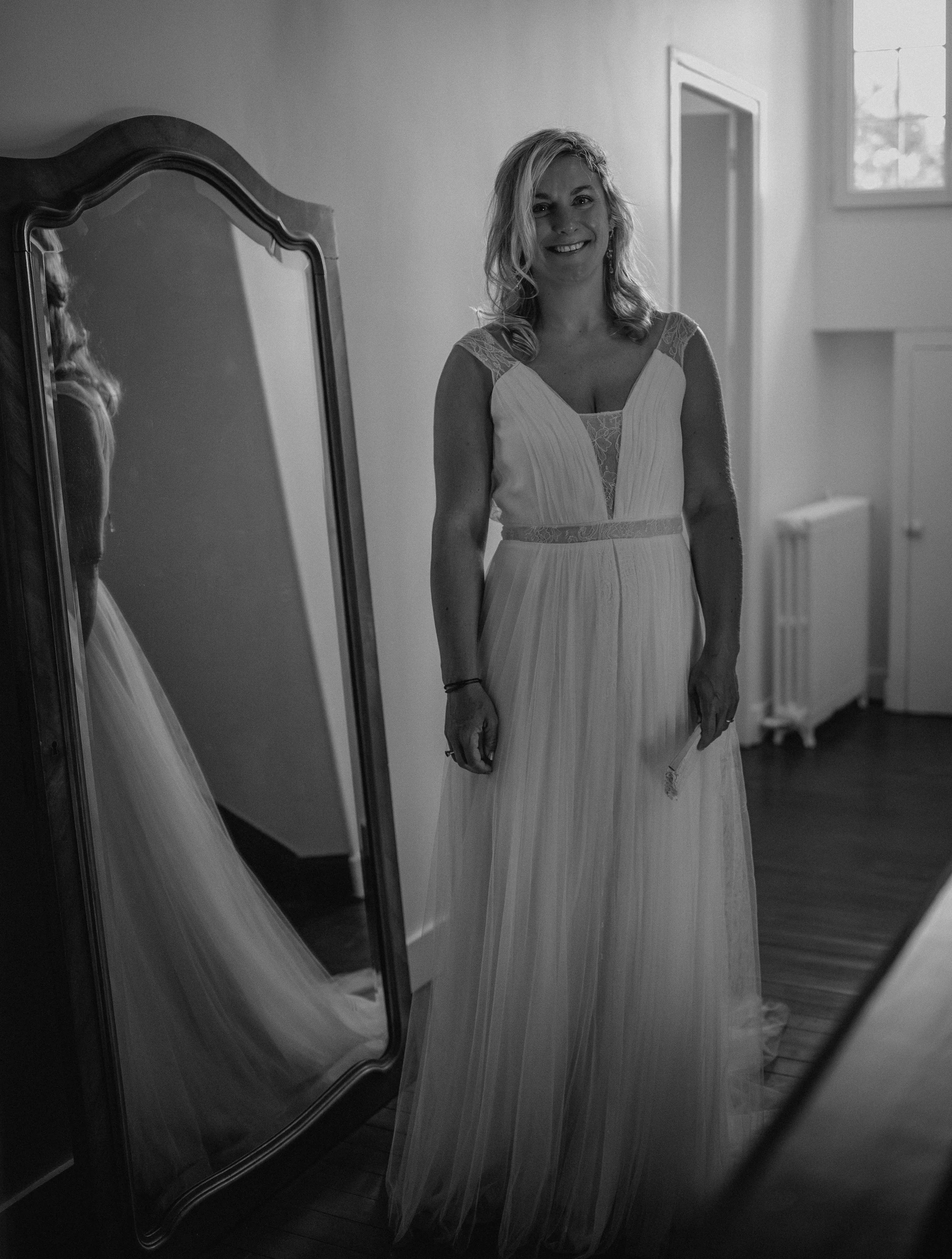 Femme portant une robe de mariée devant un miroir dans une pièce lumineuse.