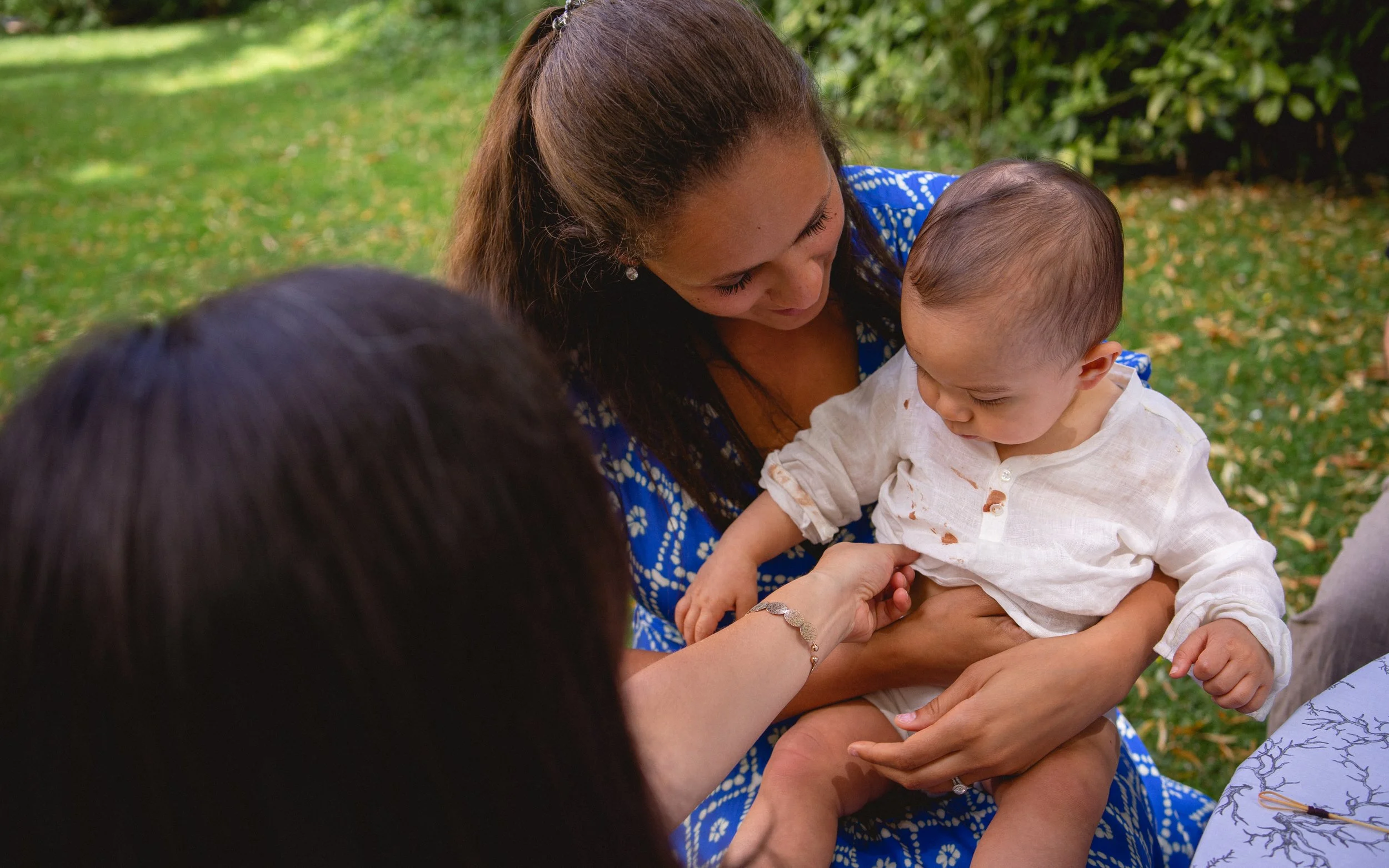 Une femme aide un jeune enfant à mettre une piqûre dans son bras, sous la supervision d'une autre personne, dans un environnement extérieur avec de la verdure.