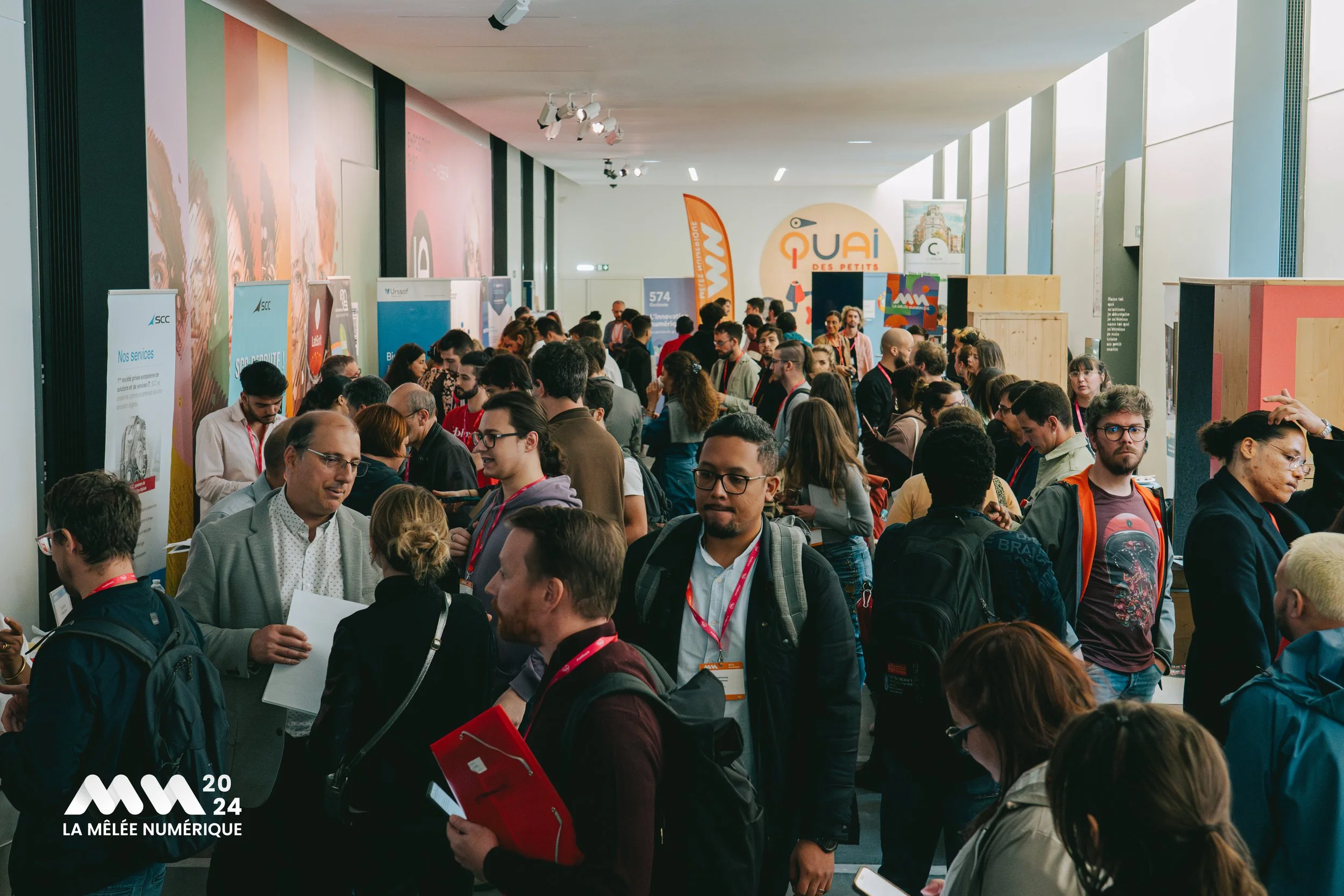 Une foule de personnes participe à une conférence ou un salon numérique, avec des stands et des banderoles aux arrière-plans.