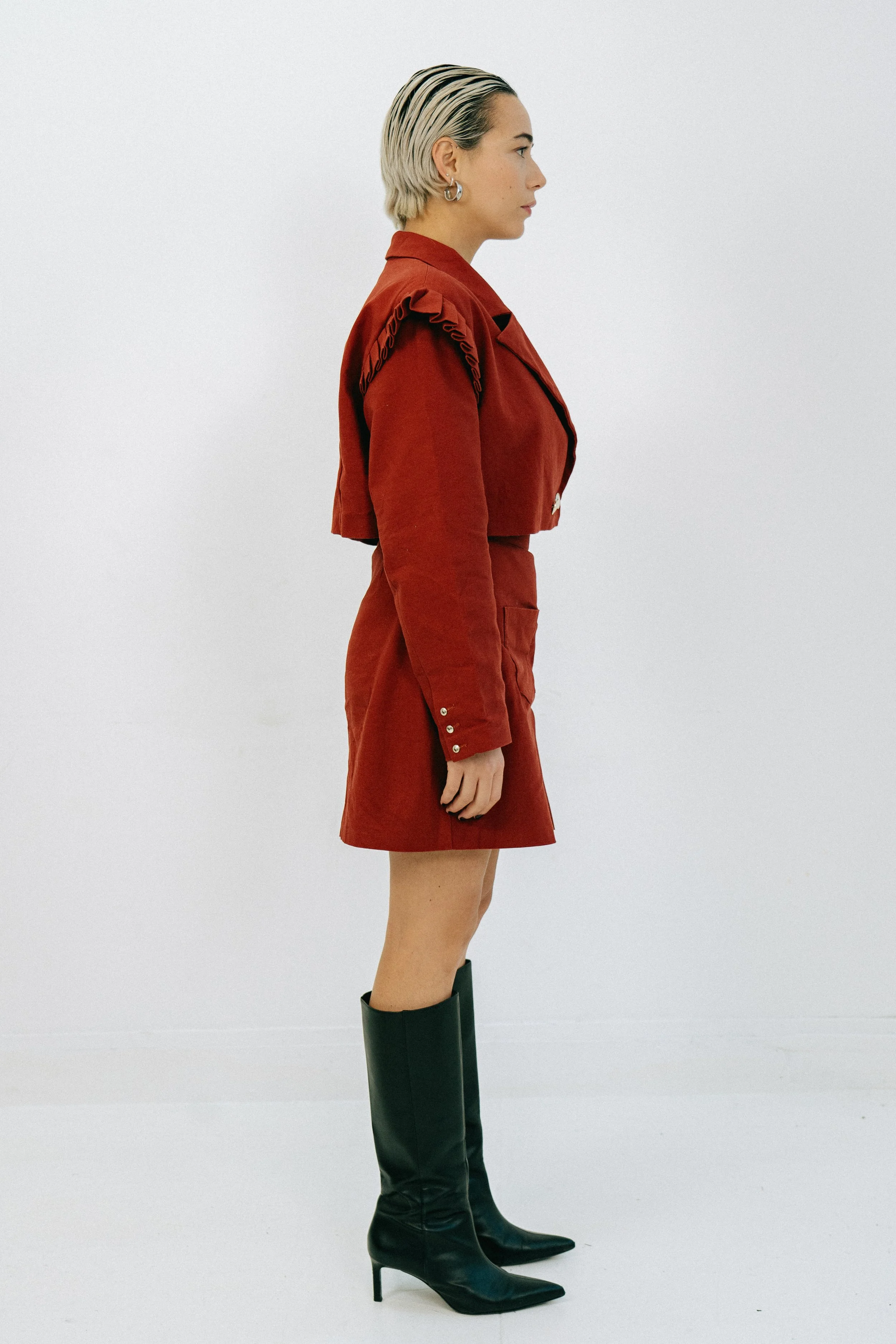 Une femme debout en profile, portant un manteau rouge avec une jupe assortie et des bottes noires hautes