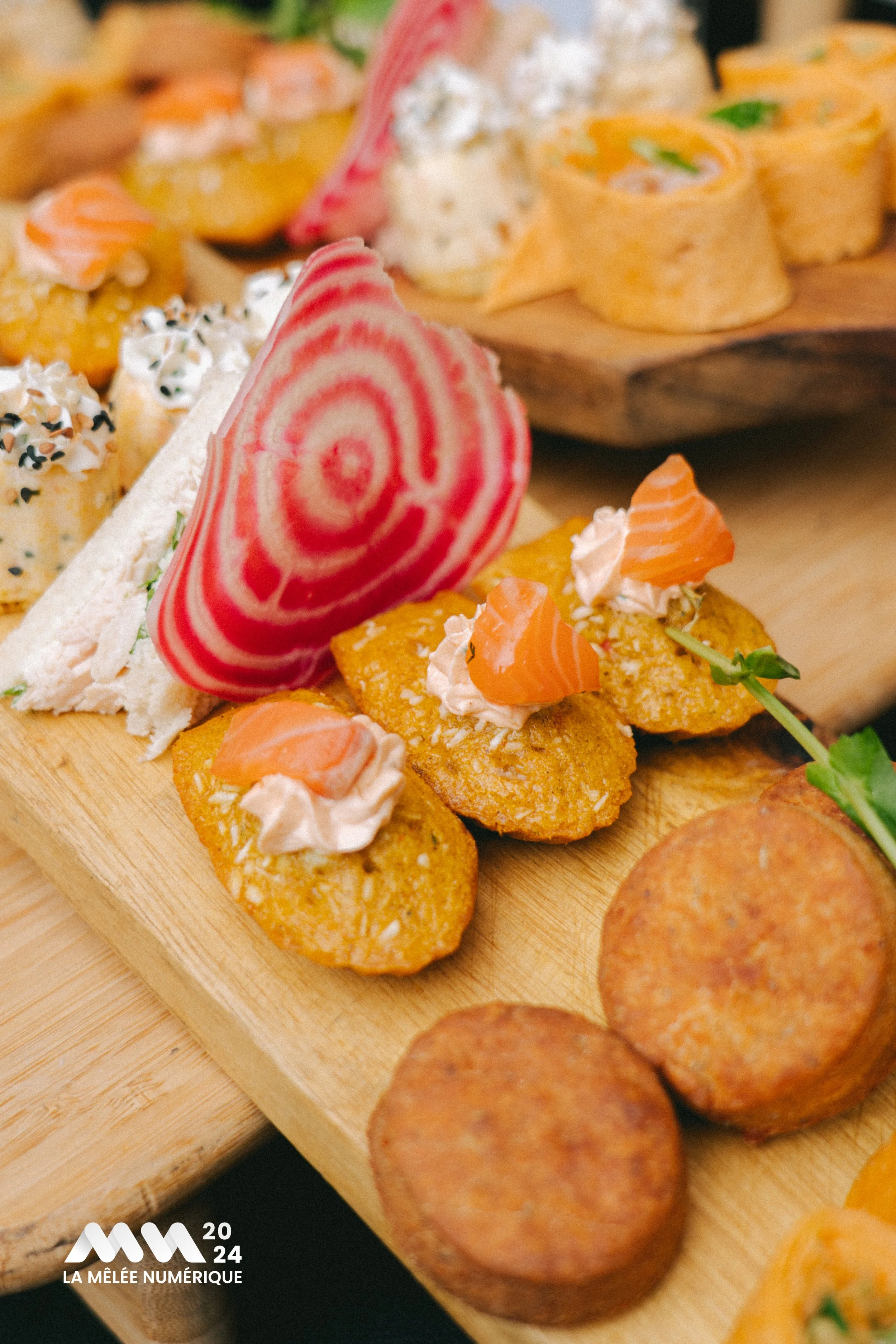 Plateau de mise en bouche avec des croquettes, des rouleaux de sushi, et une tranche de betterave décorative. Logo 
