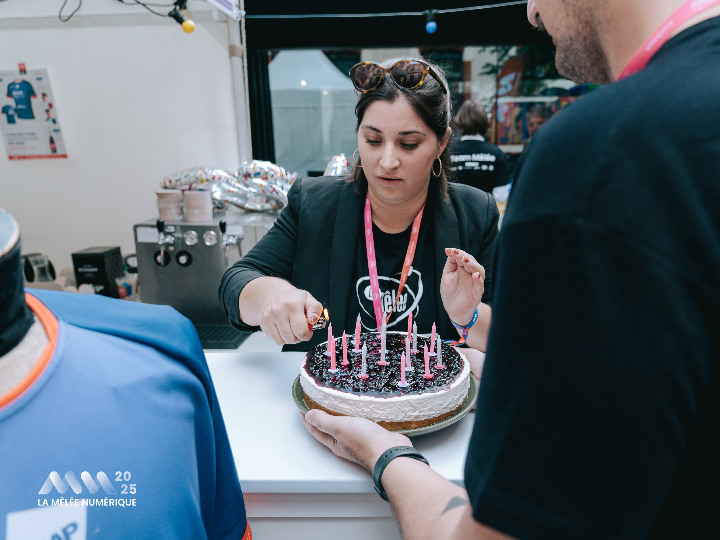 Une femme coupe un gâteau d'anniversaire avec des bougies roses, entourée de plusieurs personnes.