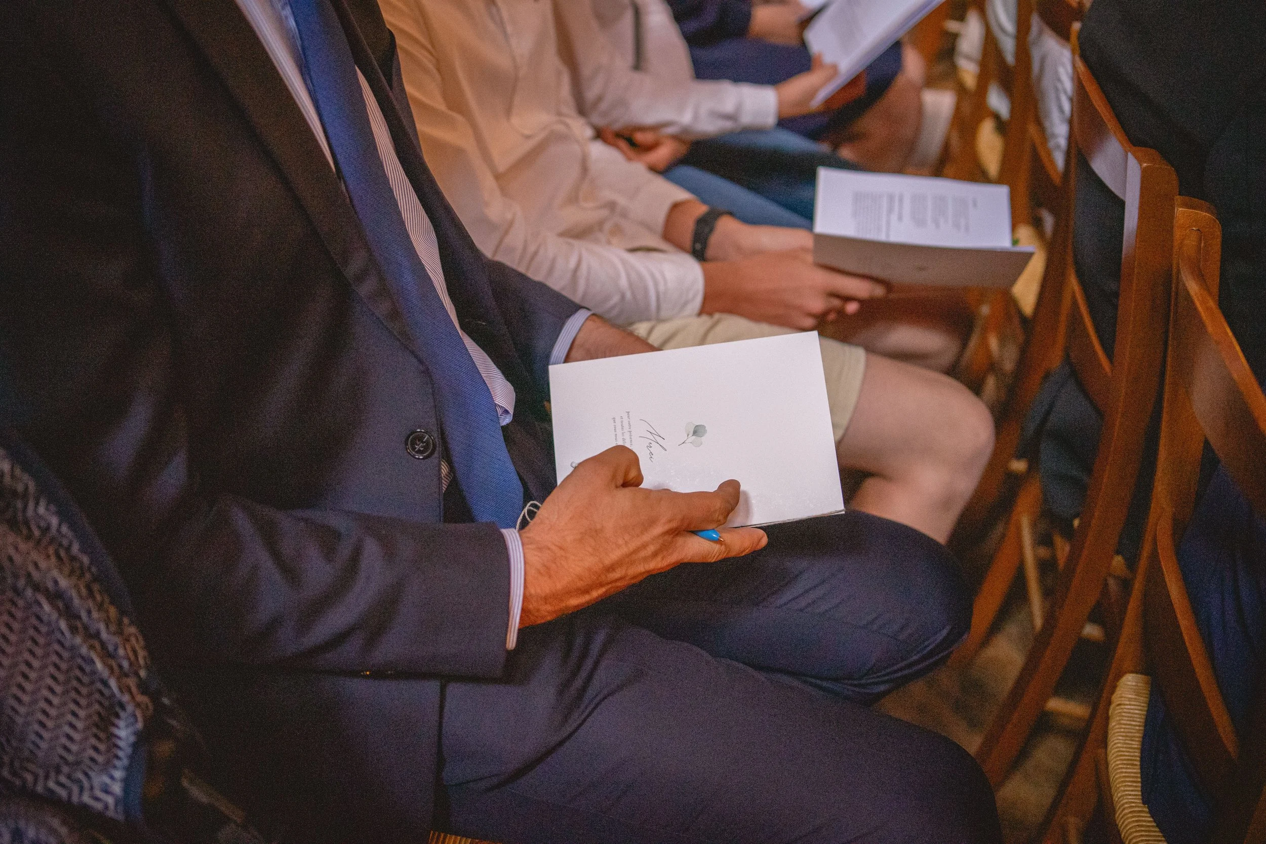 Des personnes assises dans une salle, tenant des programmes ou des documents, probablement lors d'une cérémonie ou d'une conférence.