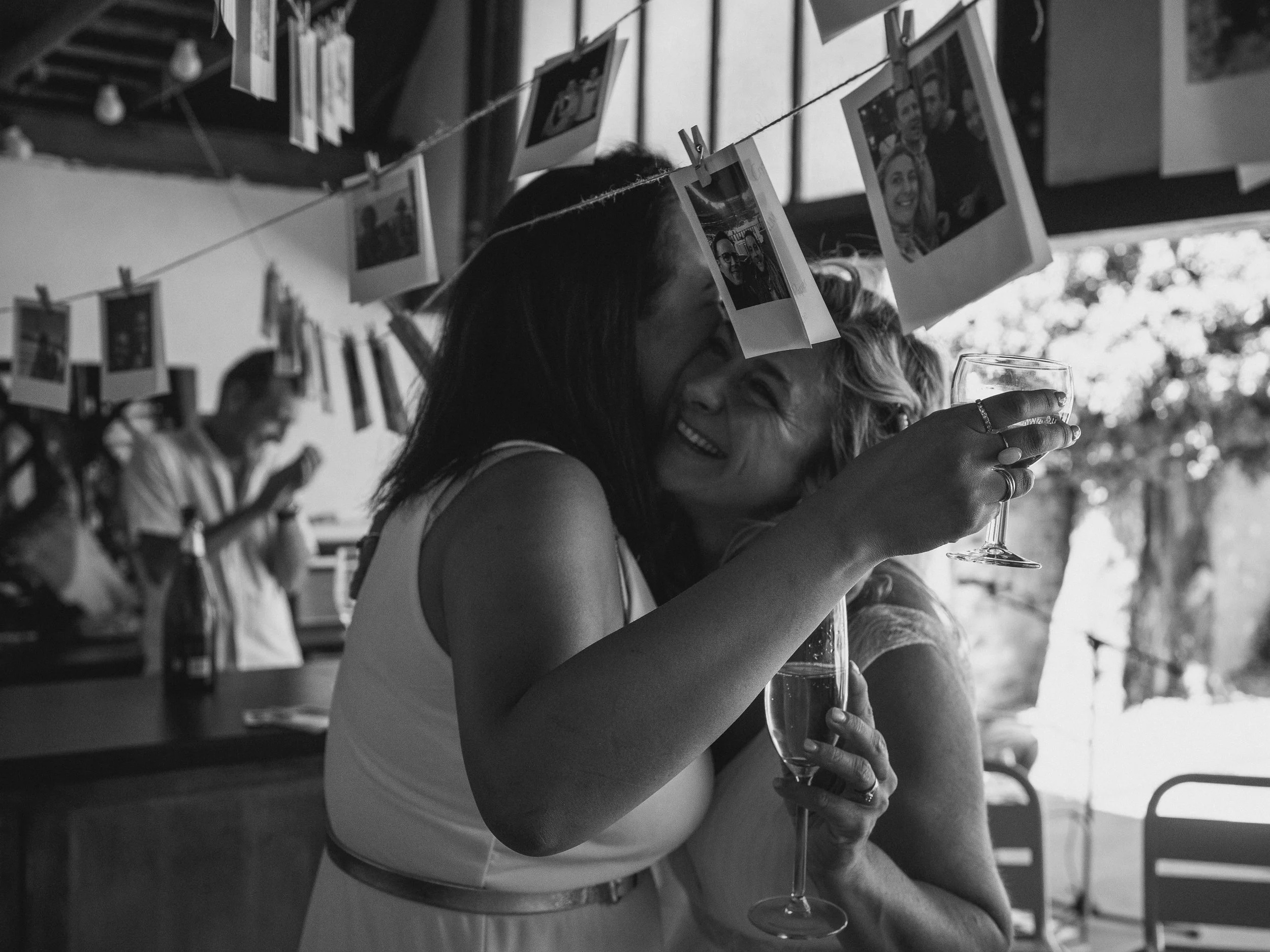 Deux femmes souriantes, célébrant avec des verres de champagne dans une fête. Décorations de photos accrochées au plafond, ambiance festive.