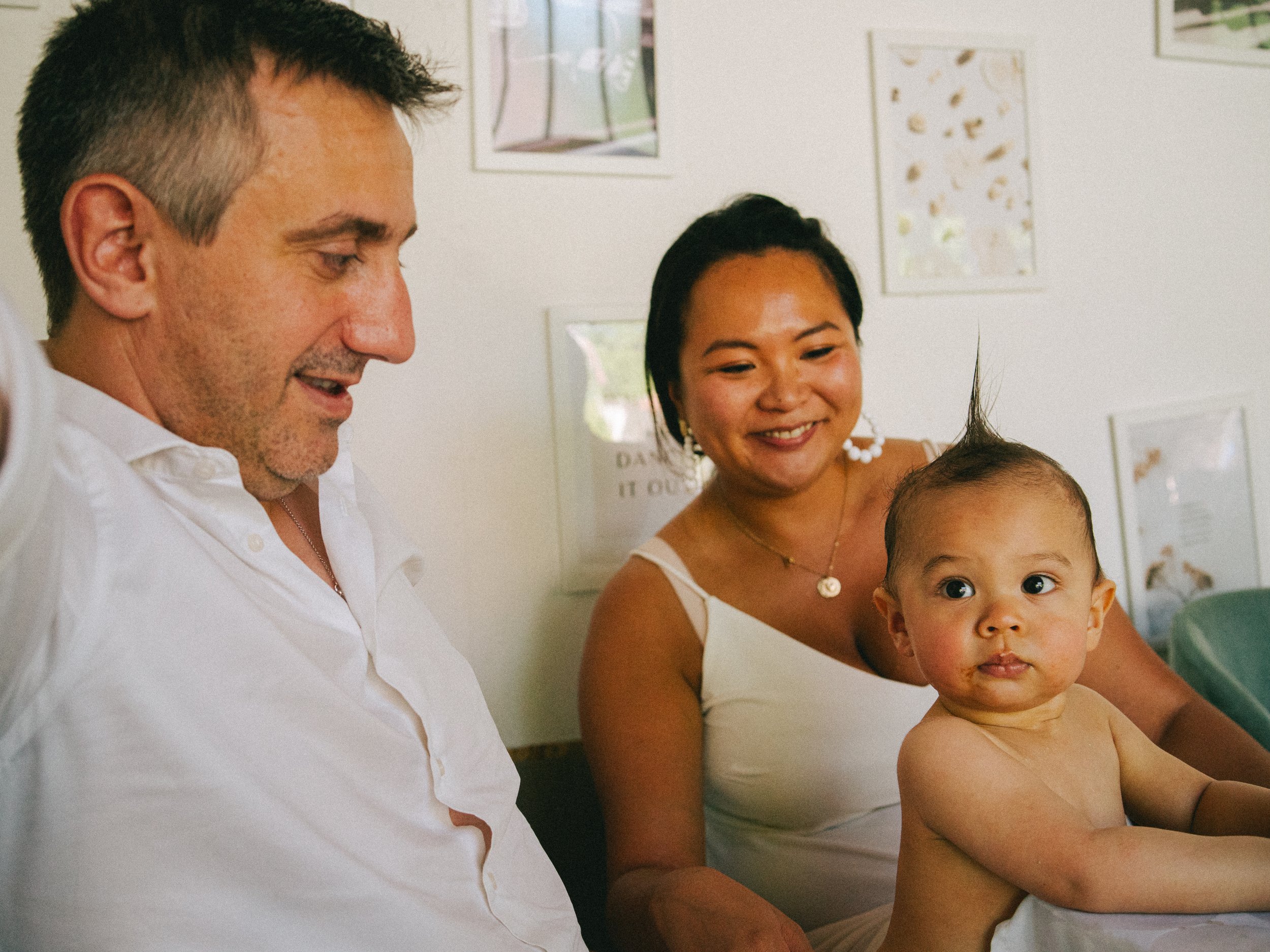 Une famille de trois personnes, un homme, une femme et un bébé, assis ensemble dans une pièce, l'air heureux.
