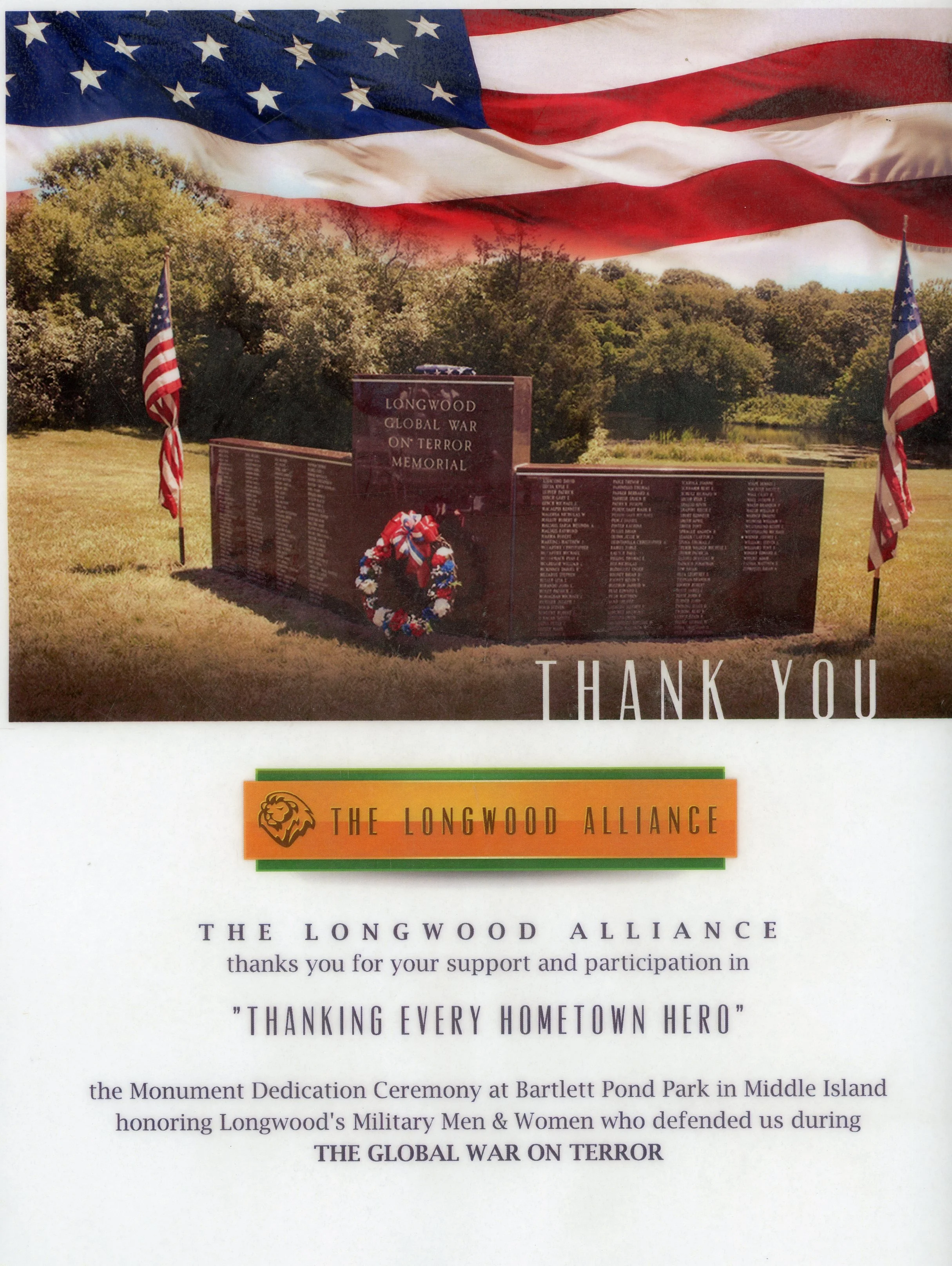 American flag flying in front of a memorial with trees and water in the background, commemorating the Longwood Global War on Terror, with additional flags and a wreath at the memorial. The text 'Thank You' and 'The Longwood Alliance' is visible.