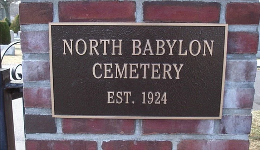 A bronze plaque on a brick wall that reads 'North Babylon Cemetery, Est. 1924'.