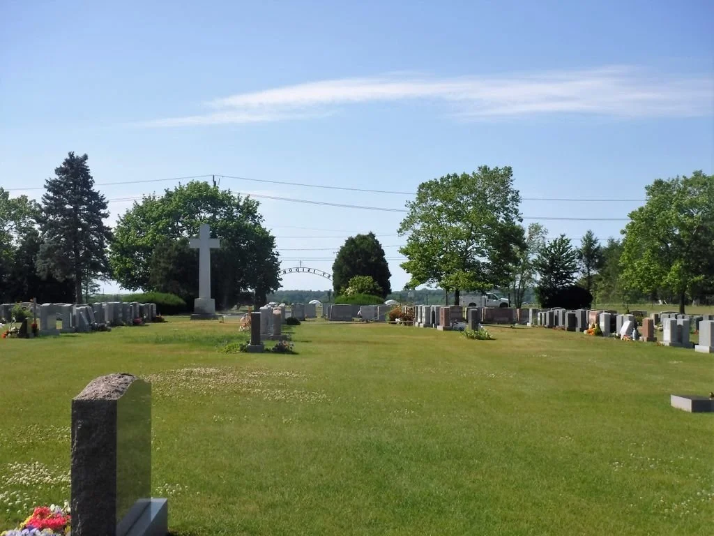 back view of cemetery with different color stones and large grey cross on the left side