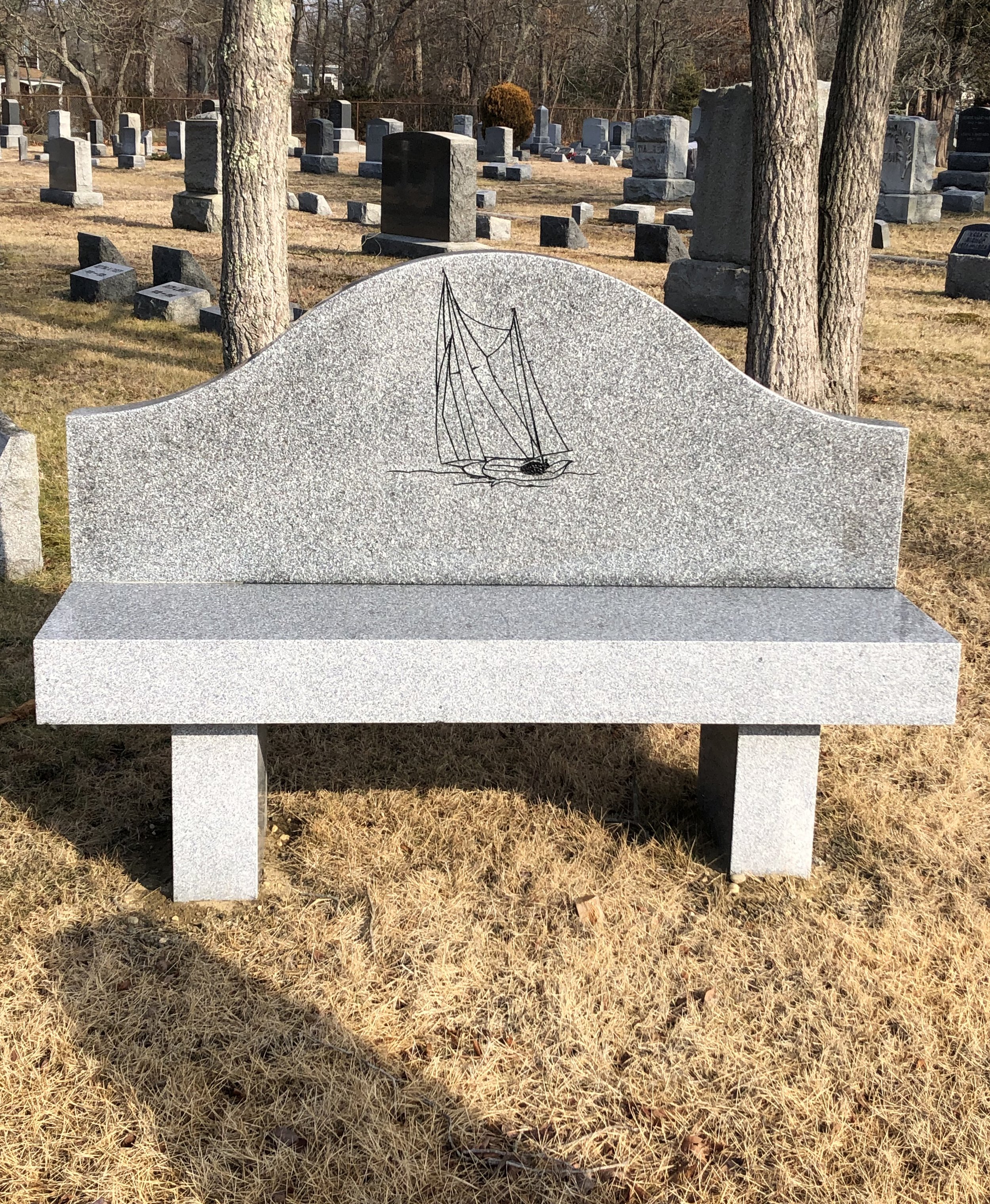 Grey bench with back in cemetery with sailboat engraved
