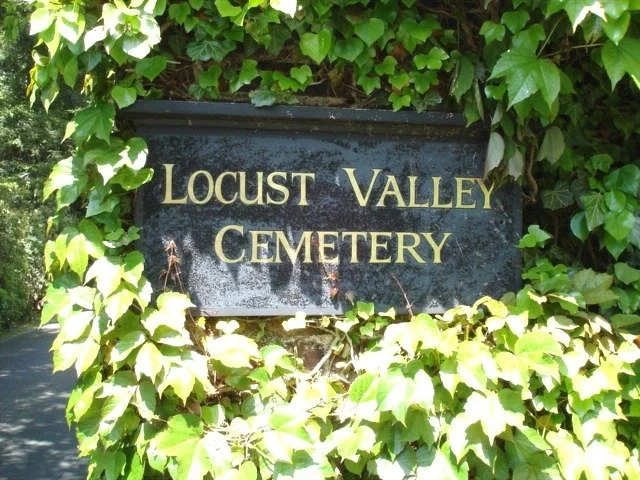 Black cemetery sign with gold lettering reading 'Locust Valley Cemetery', surrounded by green ivy leaves.