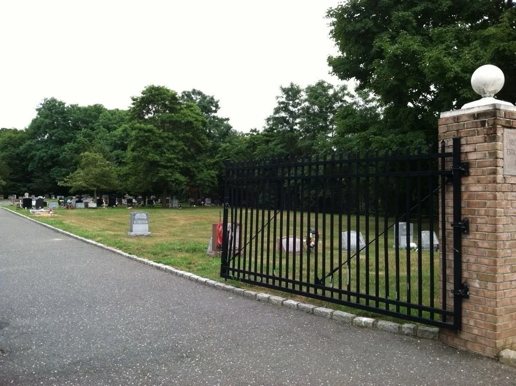 Large metal gate open and leading to cemetery with a variety of stones
