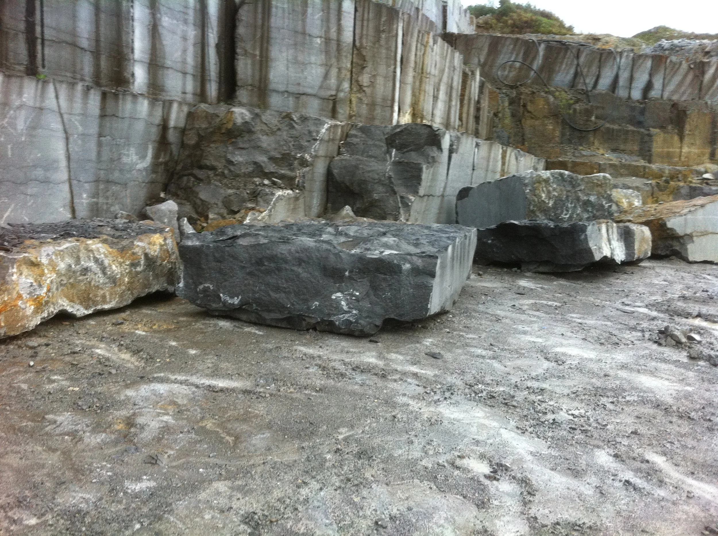 Large rocks and boulders in a rocky outdoor area with a cliff face in the background.