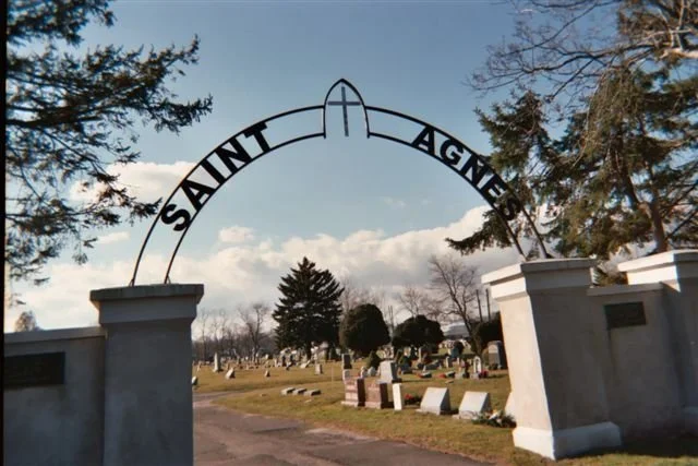 Cemetery gate with large archway, view of headstones underneath