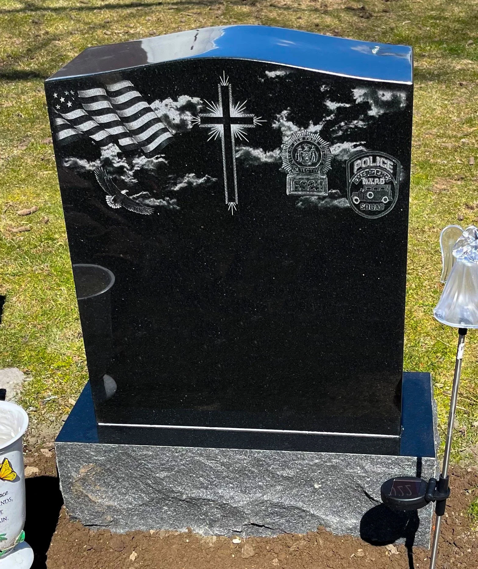 Black granite memorial with etched American flag, cross, police badge, and police emblem, set on a gray base outdoors.