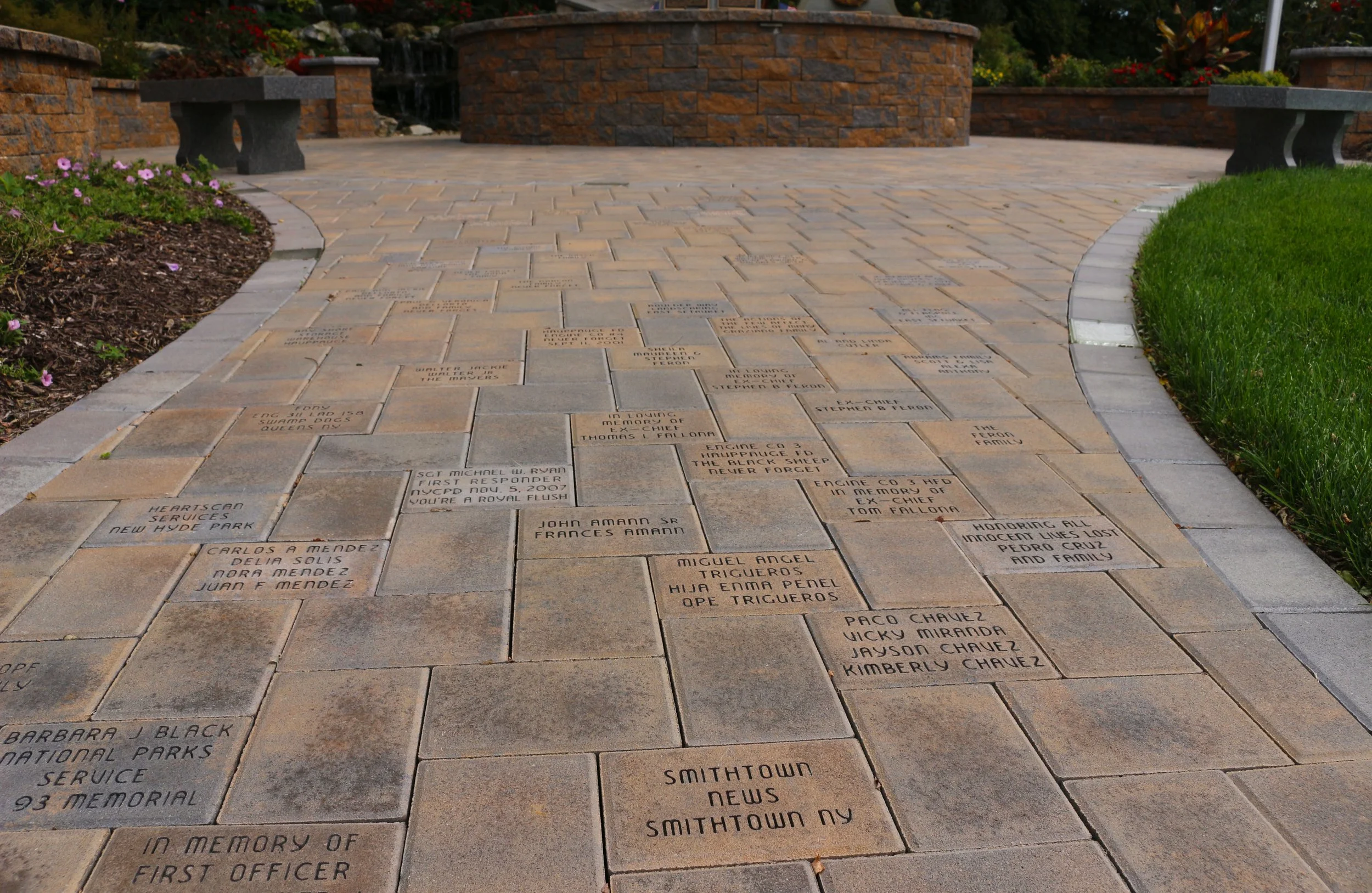 Memorial pathway with engraved bricks honoring fallen officers and service members, surrounded by flower beds and benches.