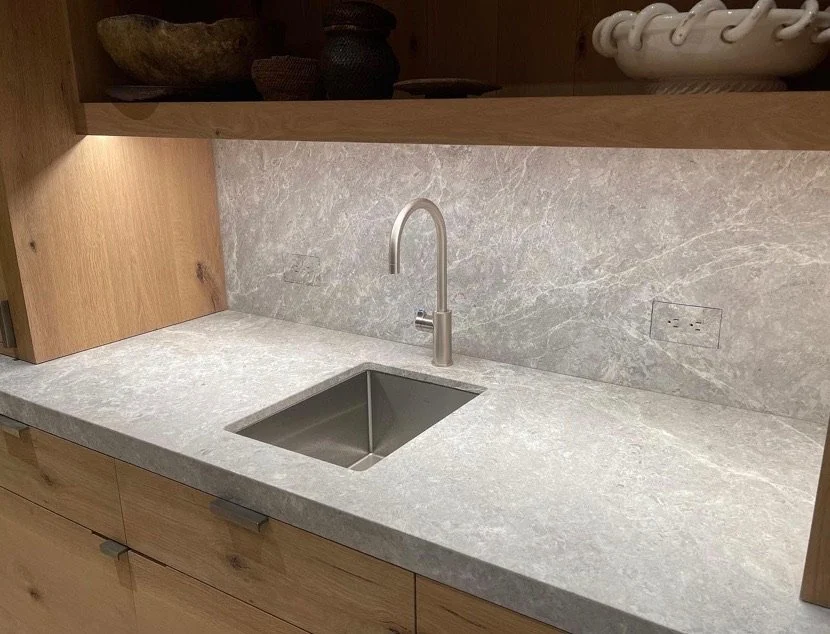 A minimalist kitchen countertop with a built-in stainless steel sink and a modern curved faucet, featuring a marble surface and wooden cabinetry.