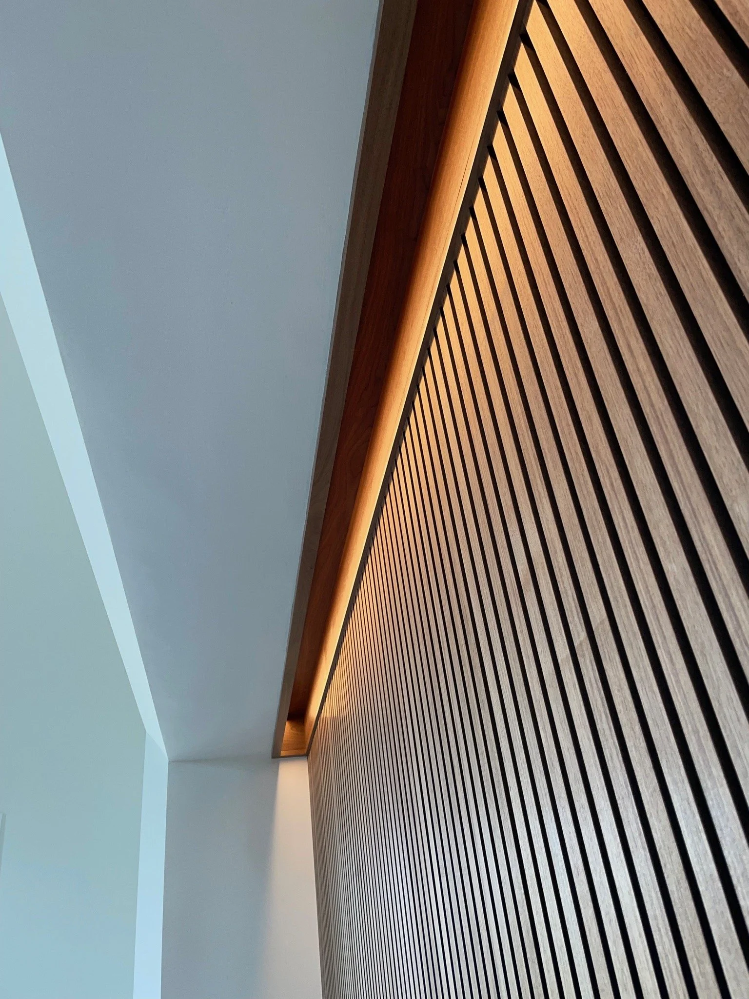 Interior ceiling with a curved wooden slat wall and modern recessed lighting.