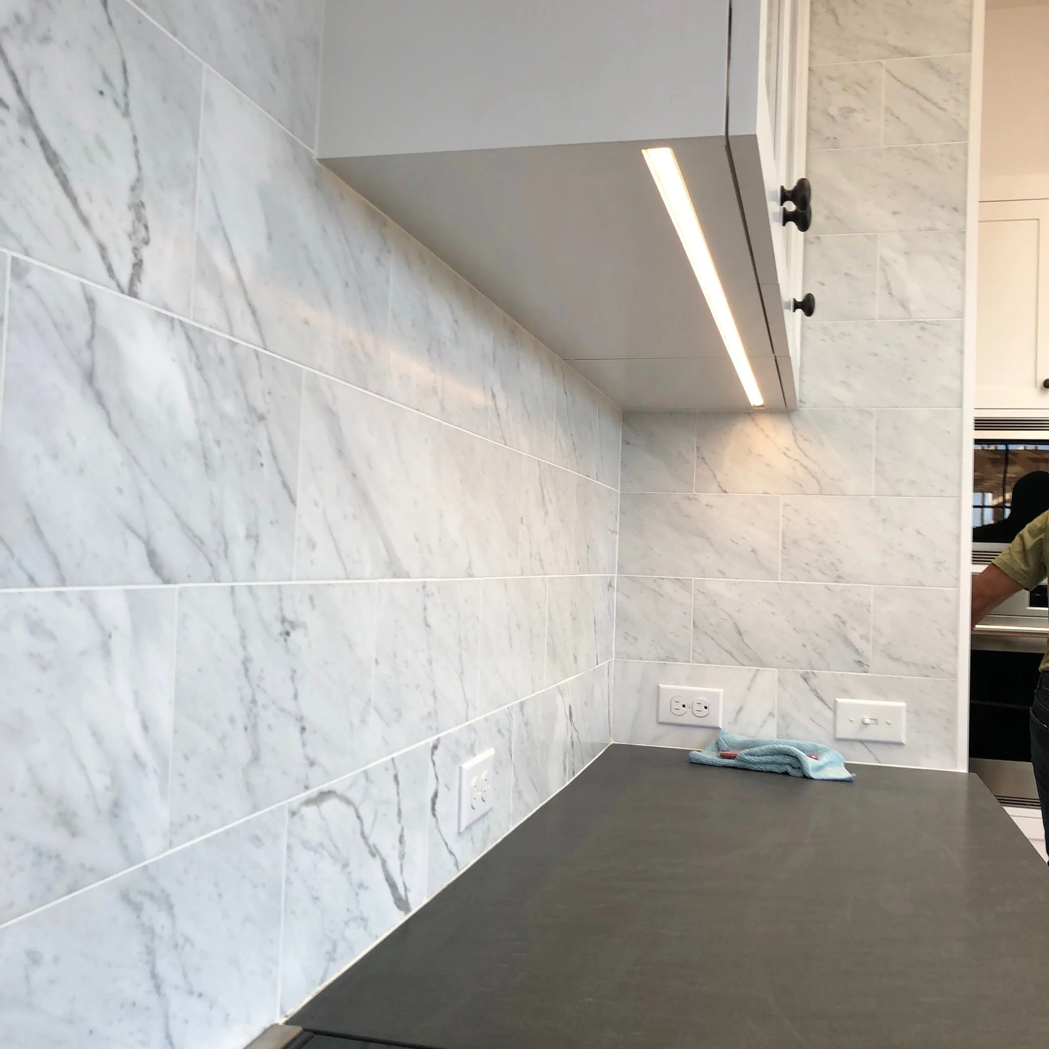 Kitchen with white marble backsplash, gray countertop, and electrical outlets, with a towel resting on the counter.