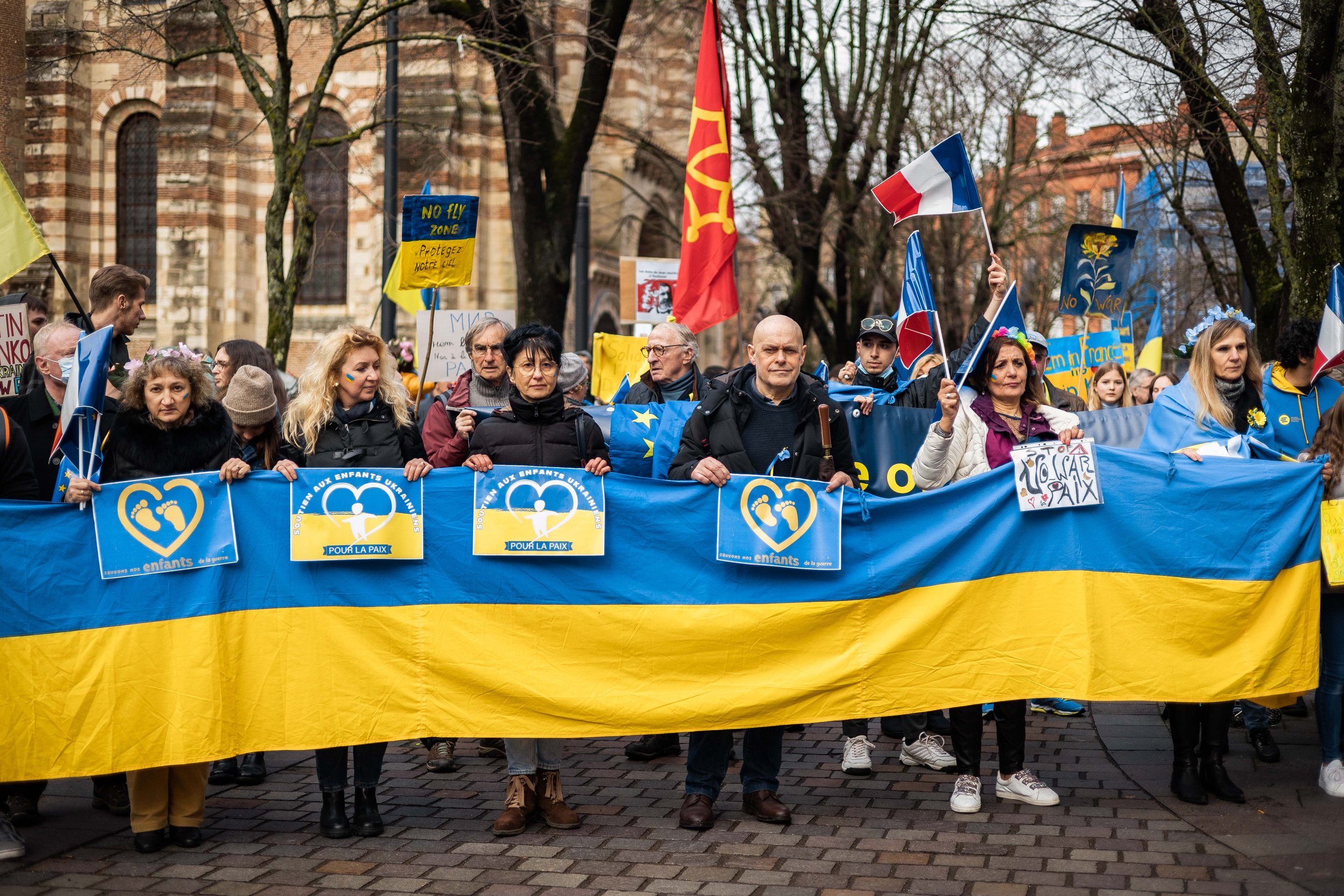Manifestation avec des personnes tenant un drapeau ukrainien et des pancartes pour la paix, avec des drapeaux français et européen en arrière-plan.