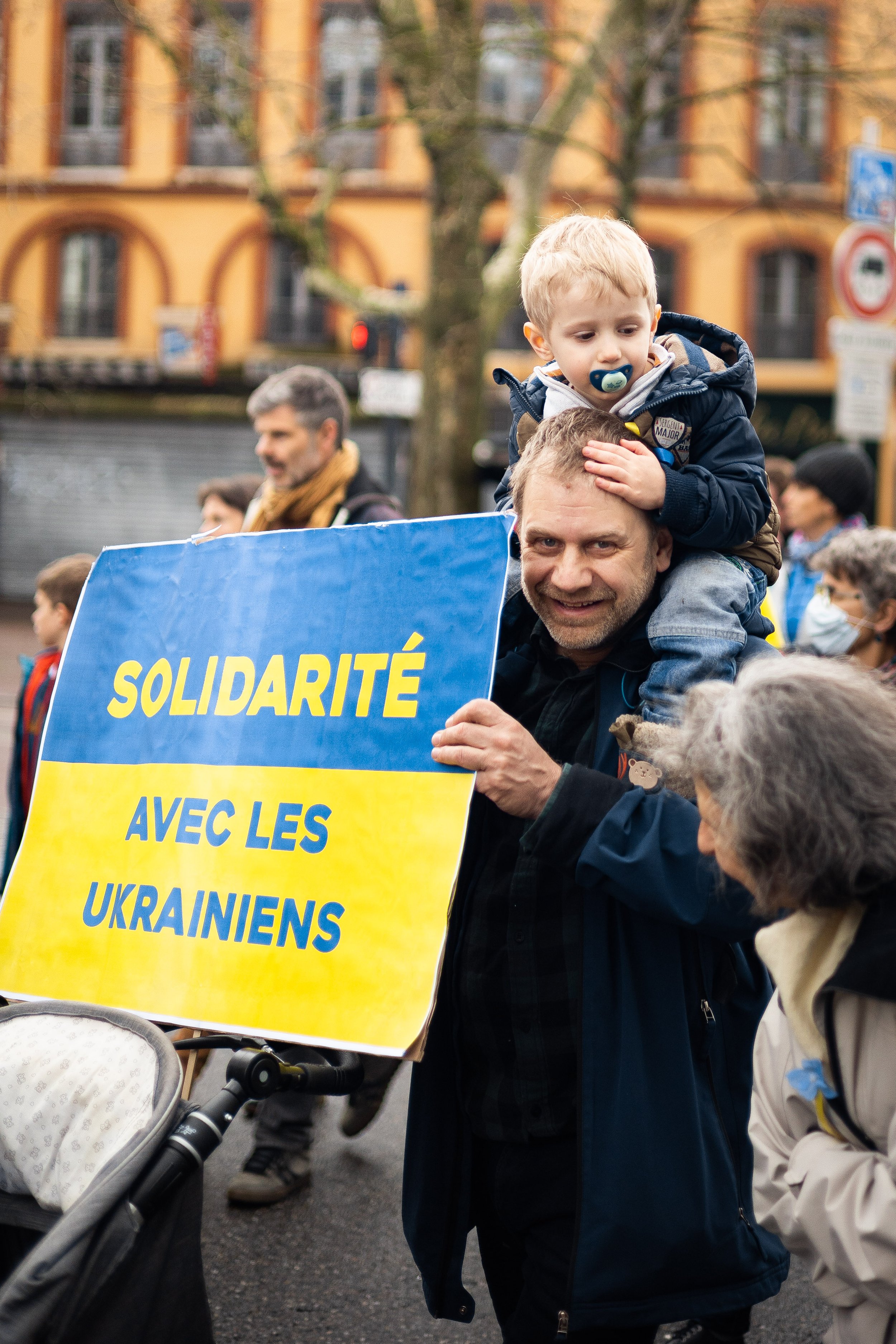 Manifestation avec une pancarte "Solidarité avec les Ukrainiens". Un homme porte un enfant sur ses épaules.