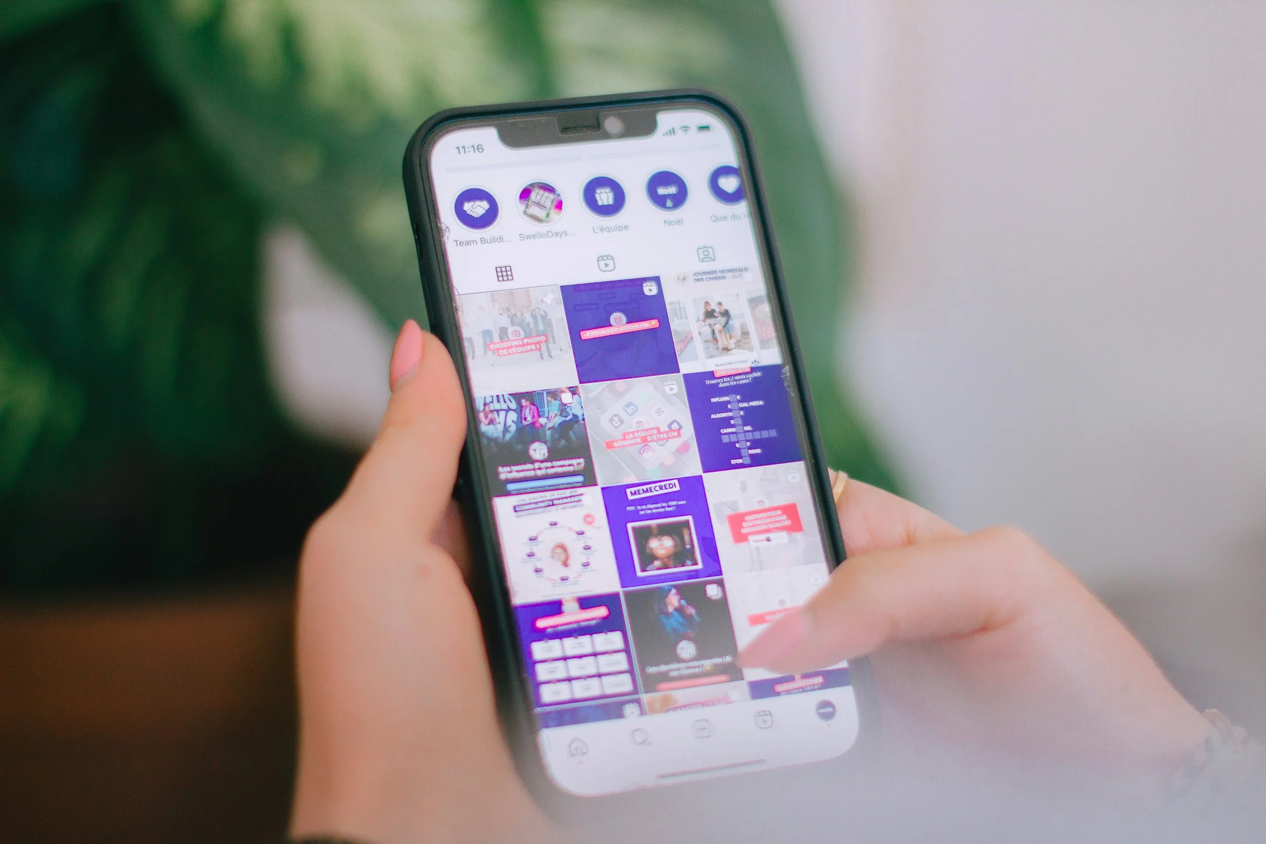 Close-up of a person holding a smartphone displaying a social media app with colorful images and icons.