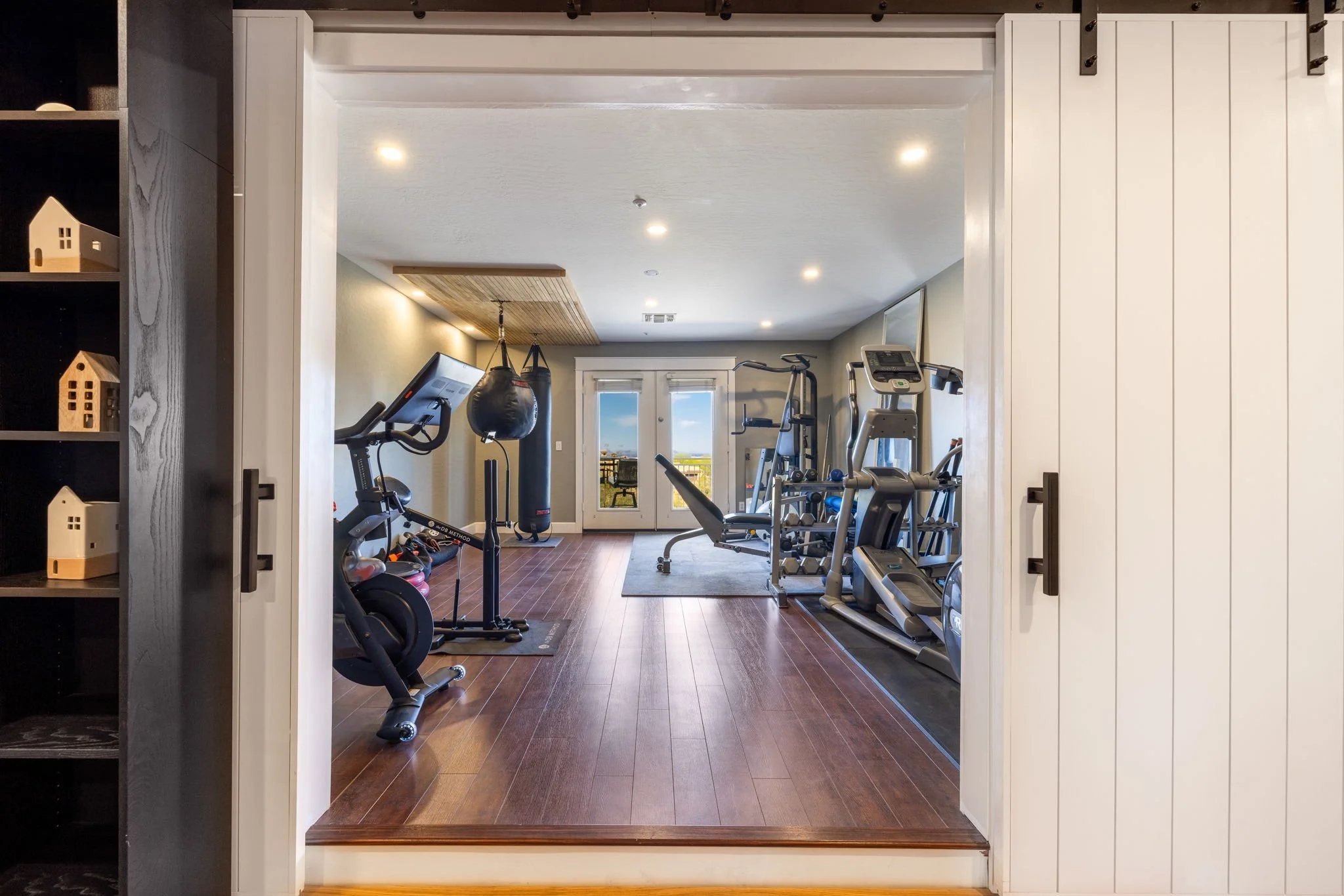 Home gym with exercise equipment including a treadmill, elliptical machine, stationary bike, punching bag, and a weightlifting bench.
