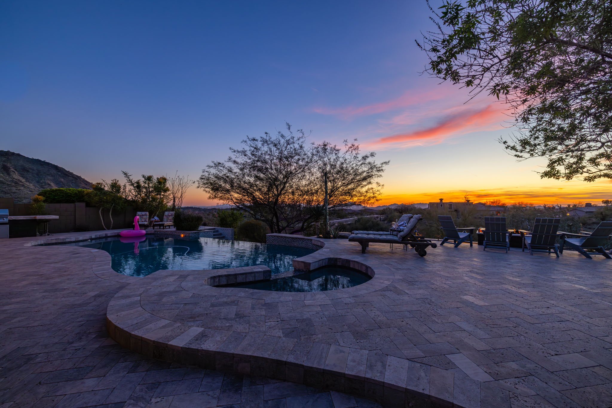 Backyard pool area during sunset with lounge chairs, trees, and a pink flamingo float in the pool.